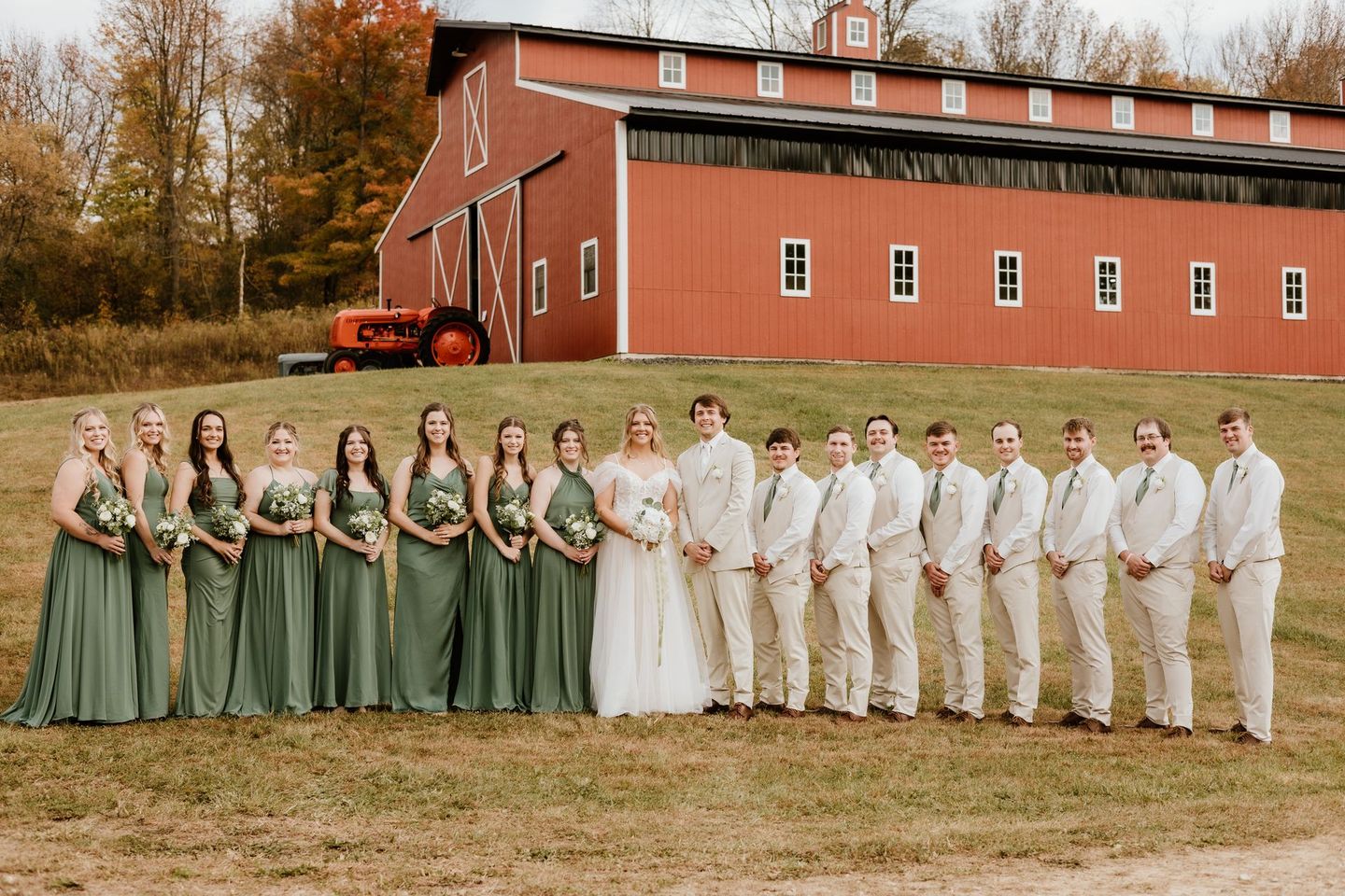 The bride and groom are posing for a picture with their wedding party in front of a red barn.