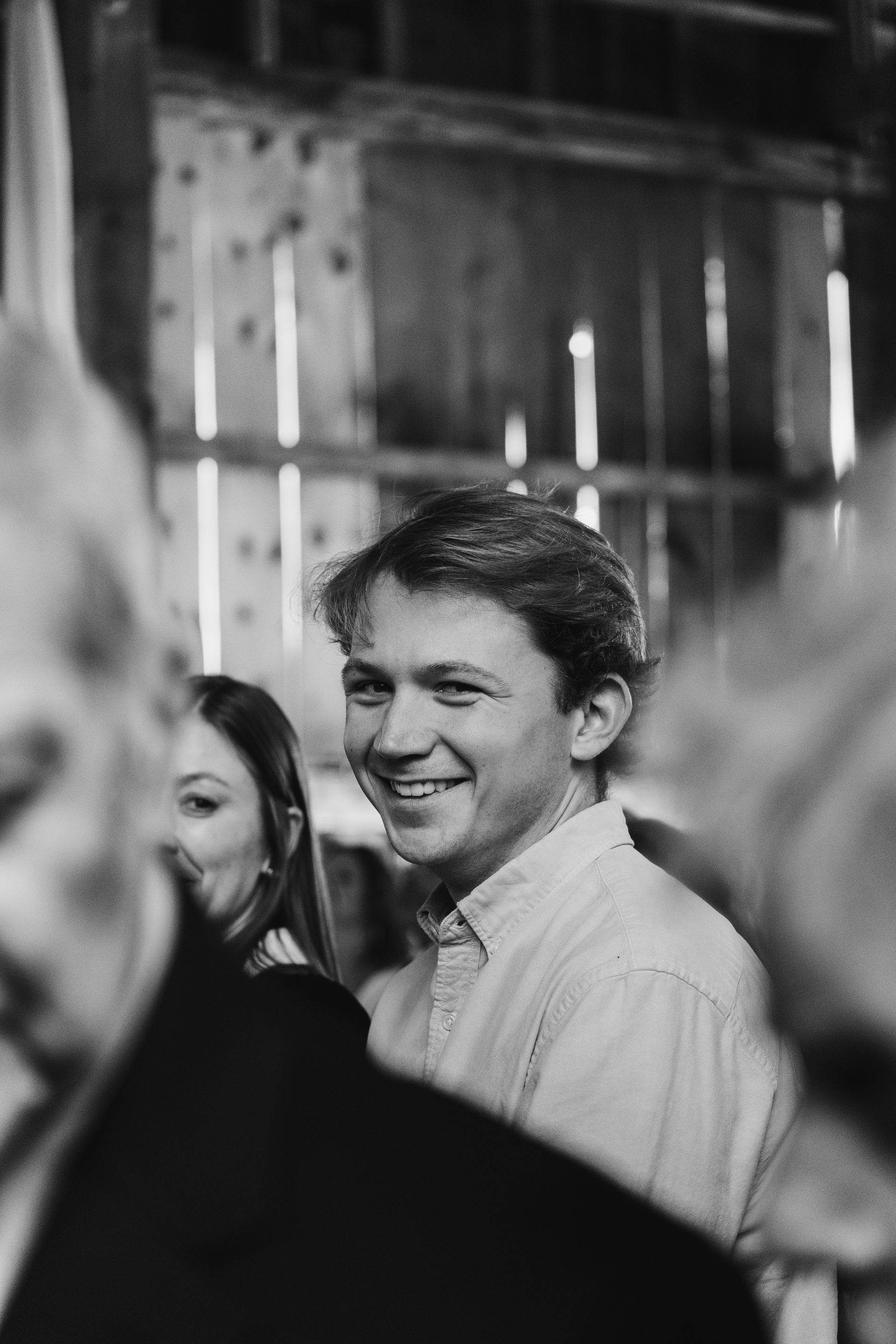 A man is smiling in a black and white photo while standing in a crowd of people.