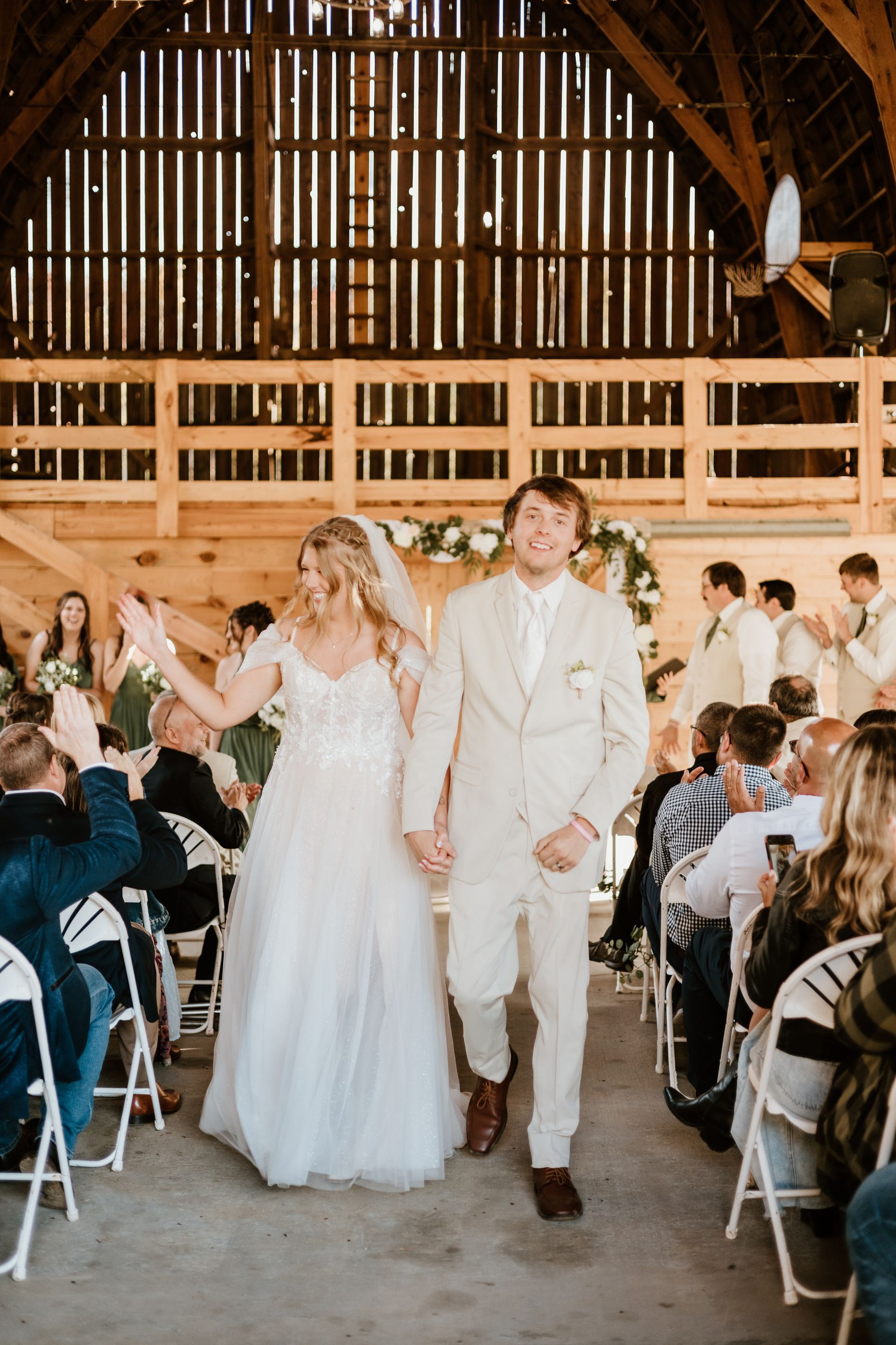 A bride and groom are walking down the aisle at their wedding in a barn.