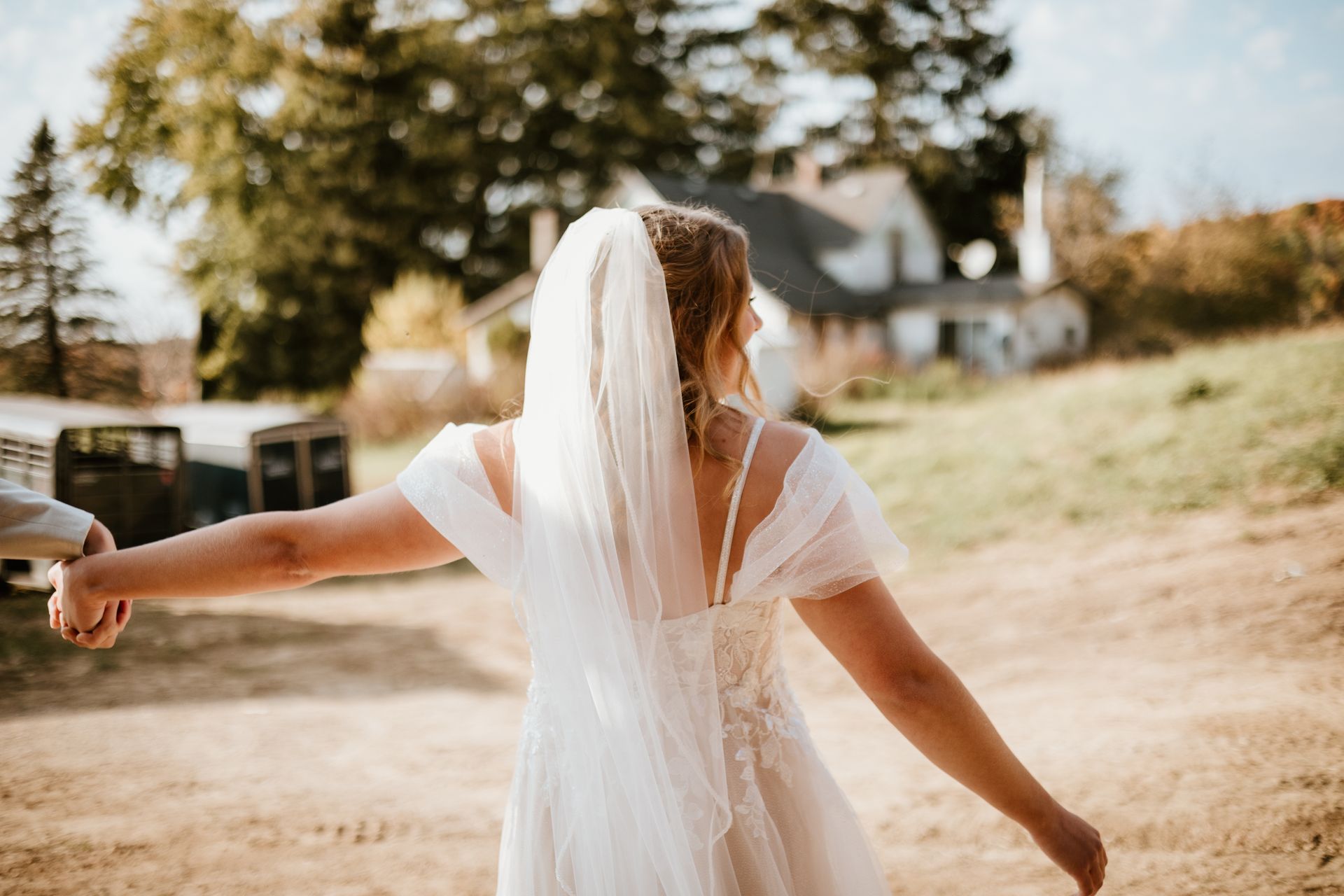 A bride and groom are holding hands and walking down a dirt road.