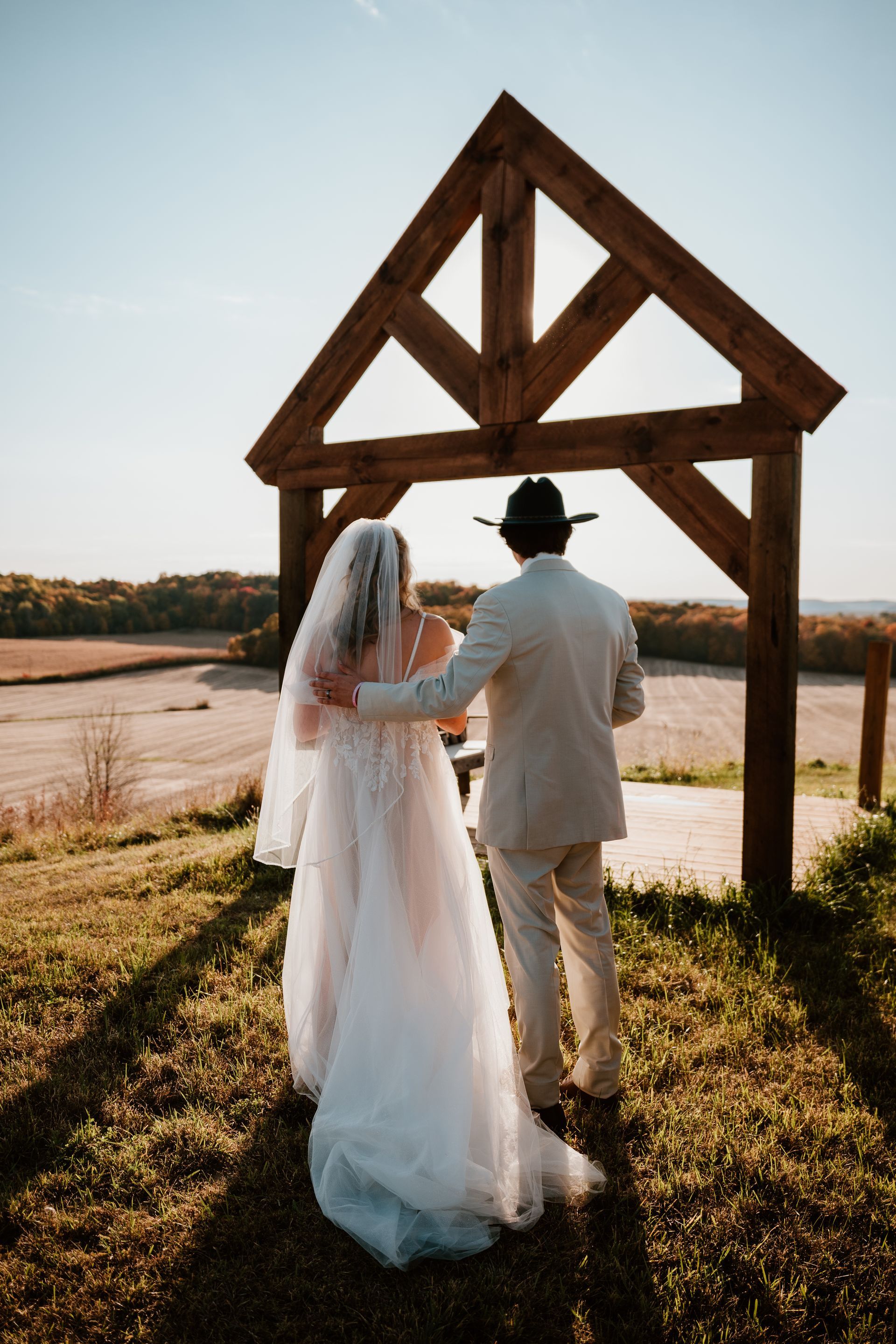 A bride and groom are walking in front of a wooden structure.