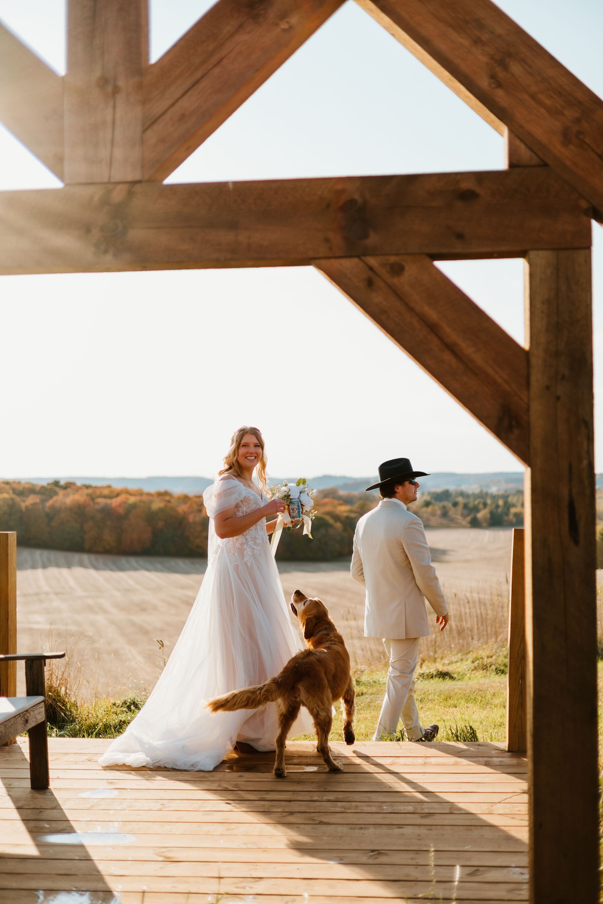 A bride and groom are standing on a wooden deck with their dog.