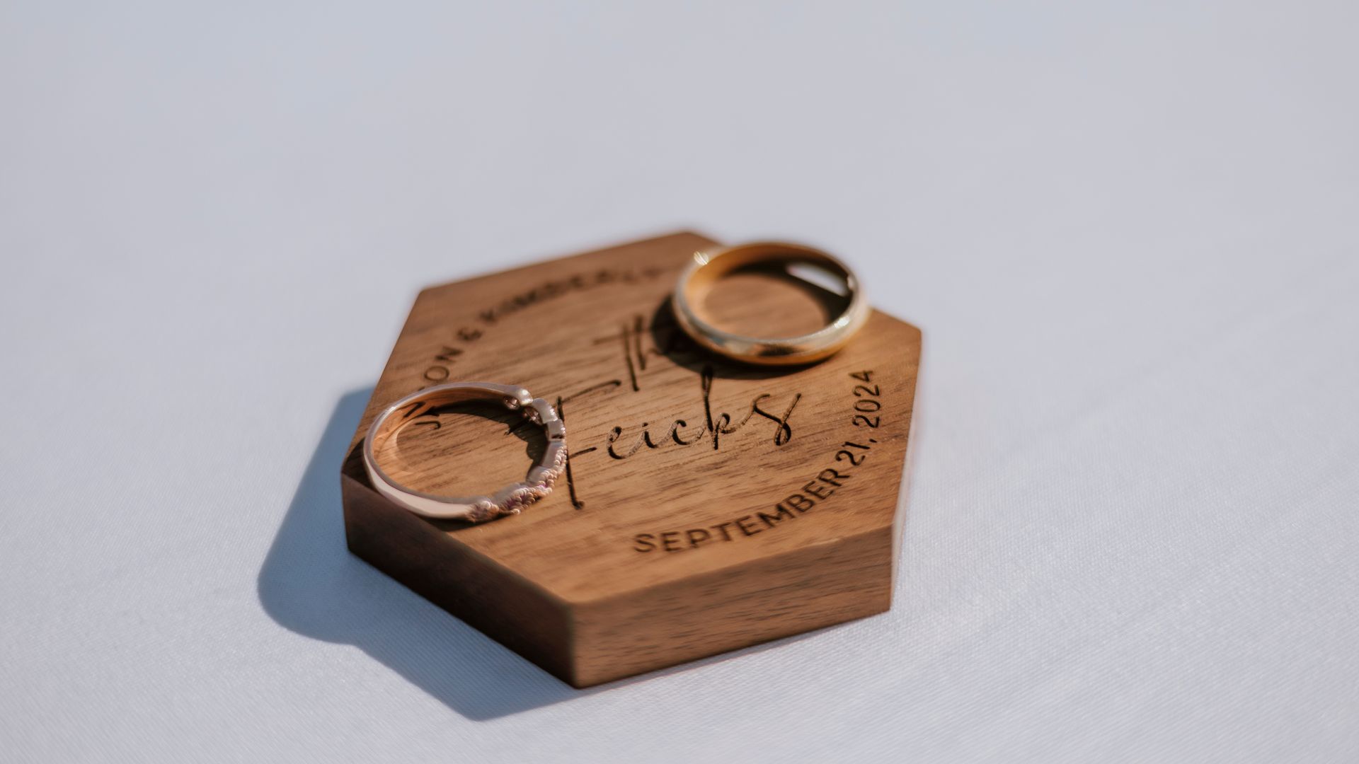 Two wedding rings are sitting on top of a wooden ring holder.