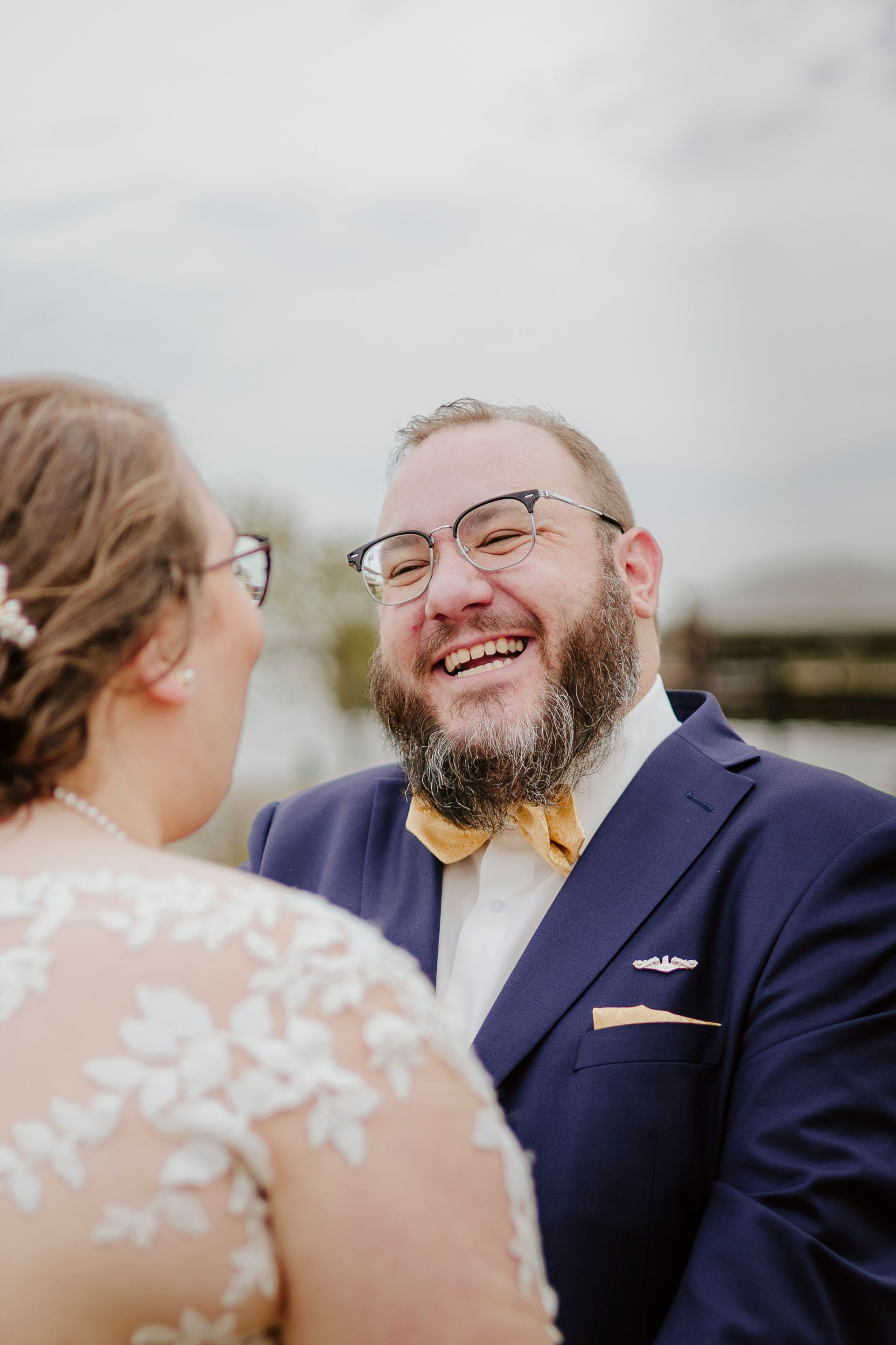 A man in a suit and bow tie is laughing with a woman in a wedding dress.