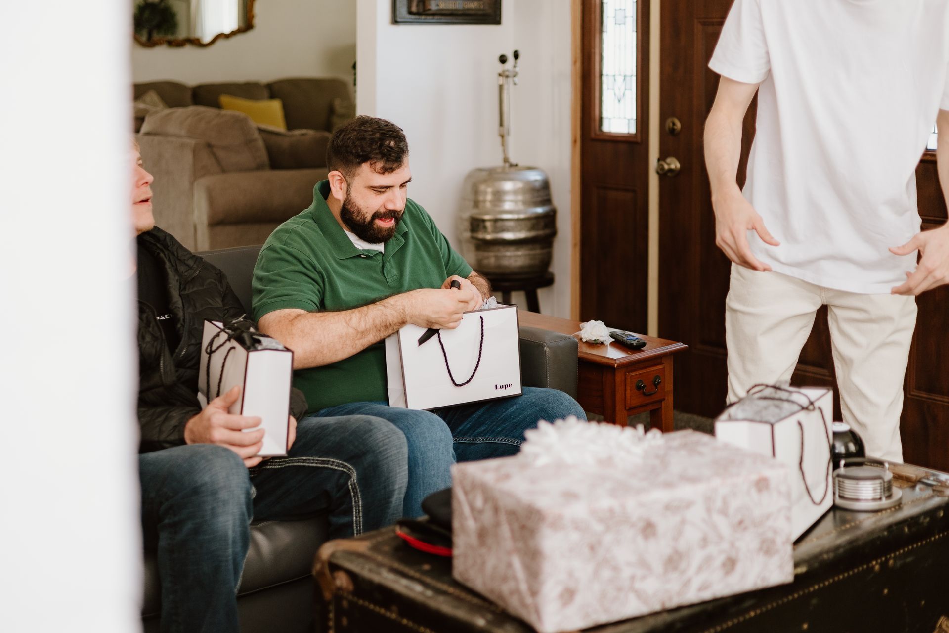 A group of men are sitting on a couch in a living room holding gifts.