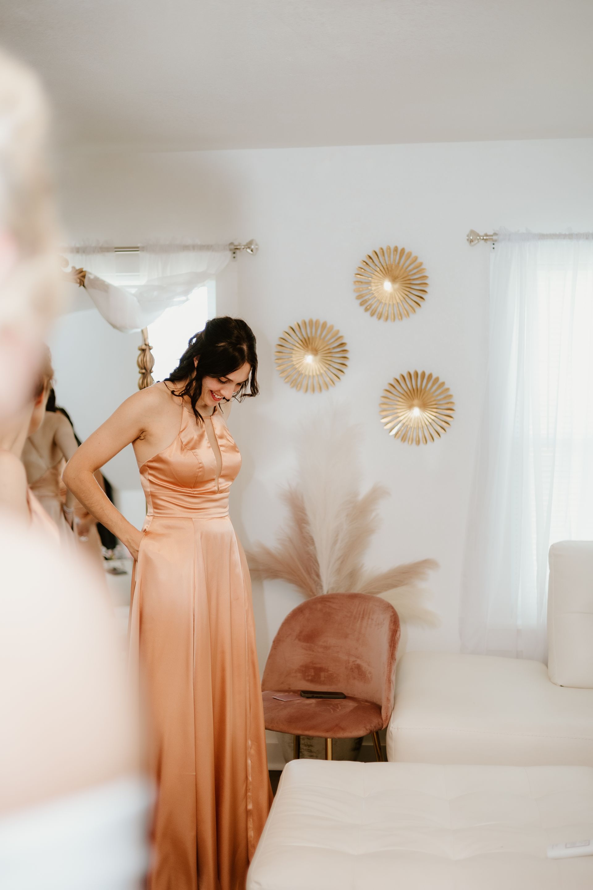 A woman in a long dress is standing in front of a mirror in a room.