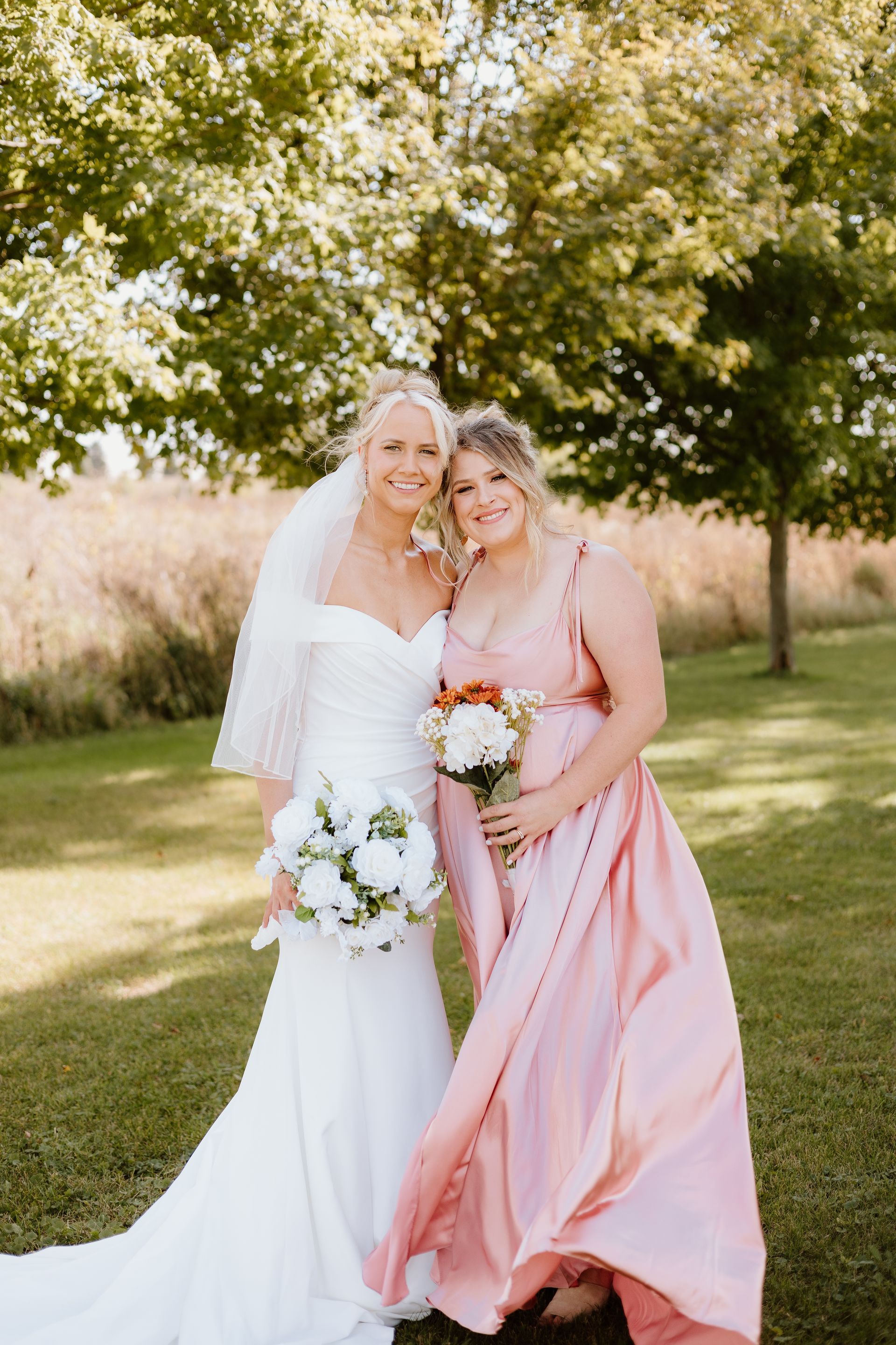 A bride and her bridesmaid are posing for a picture in a field.