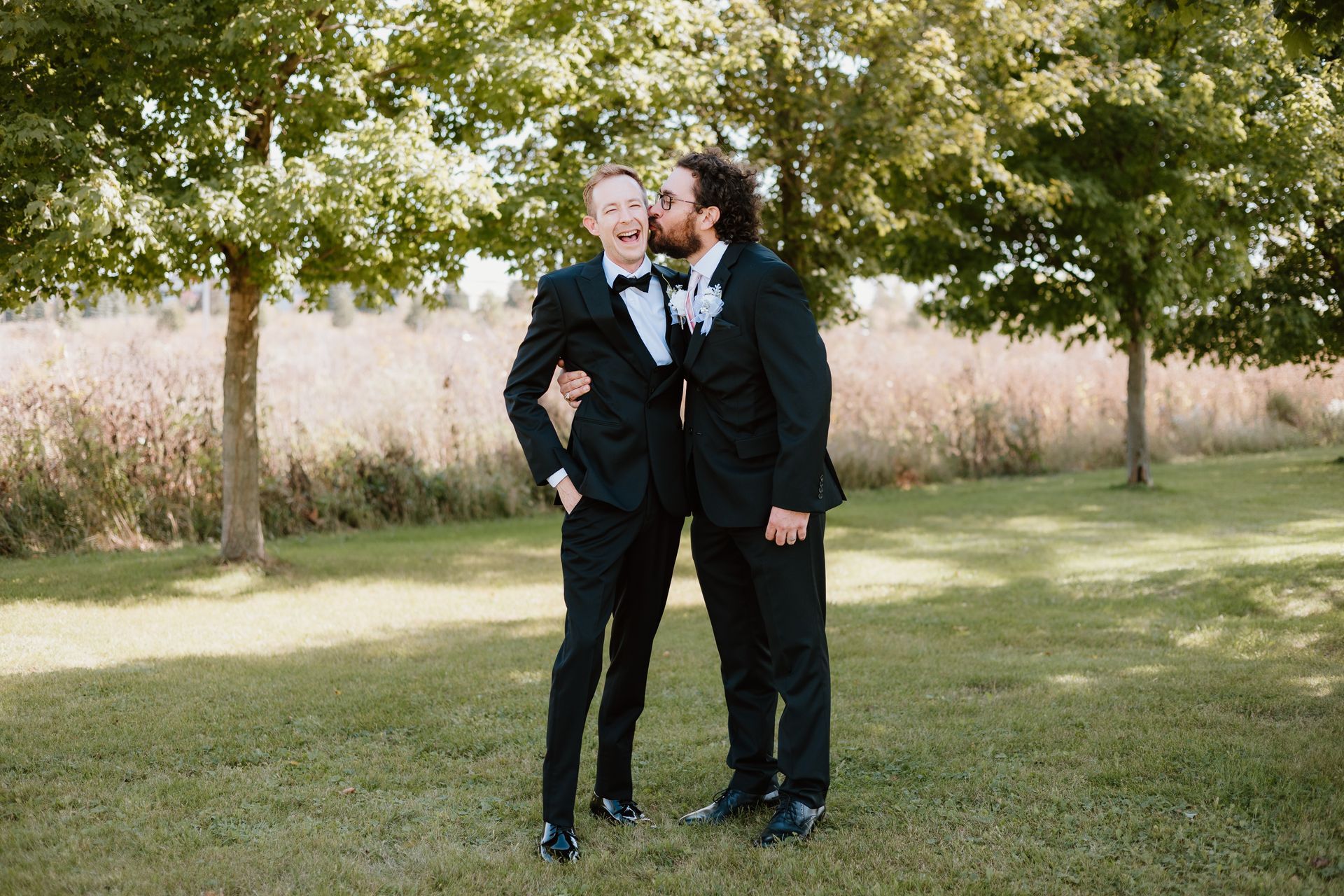 Two men in tuxedos are standing next to each other in a field.