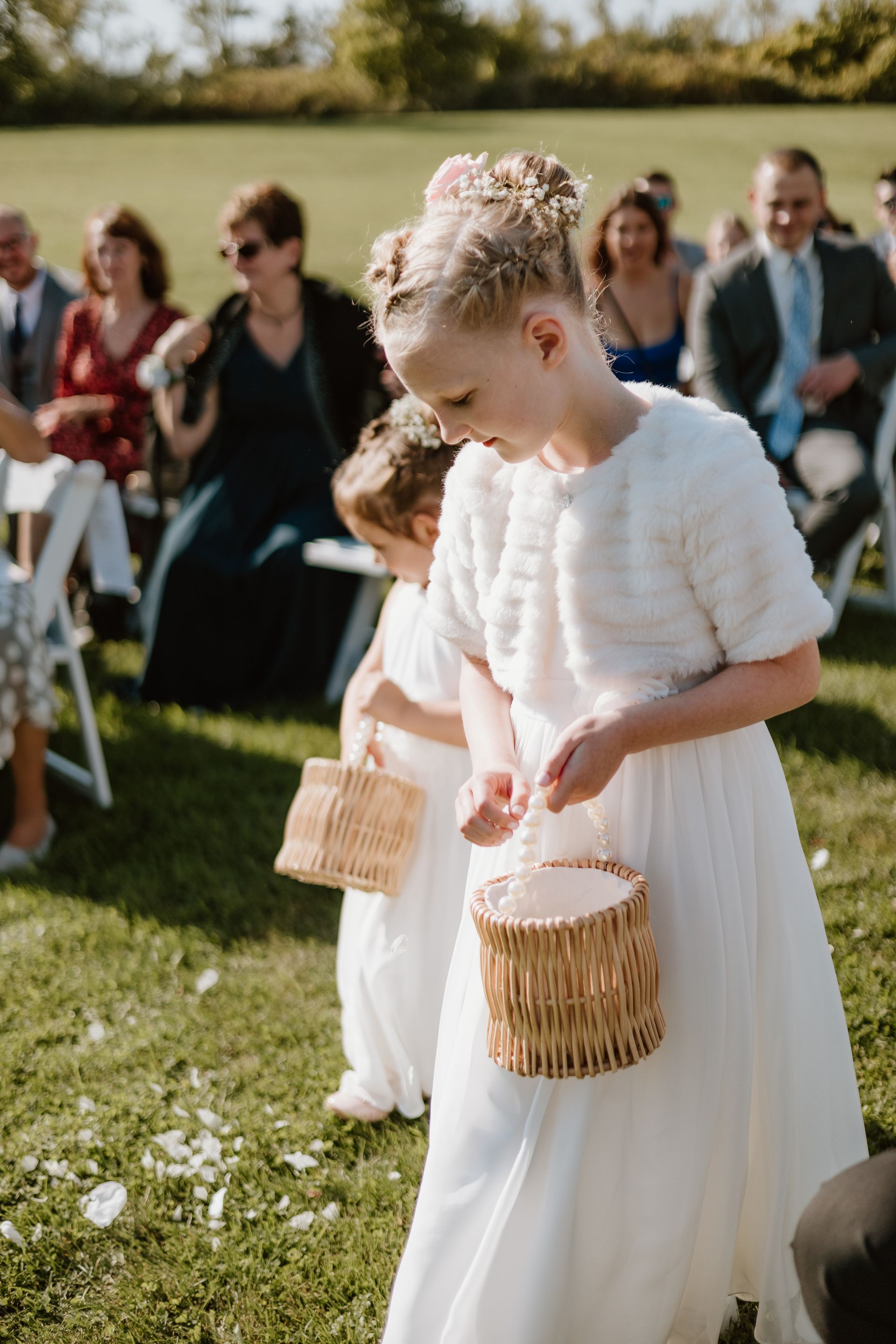 Two flower girls are walking down the aisle at a wedding holding baskets.