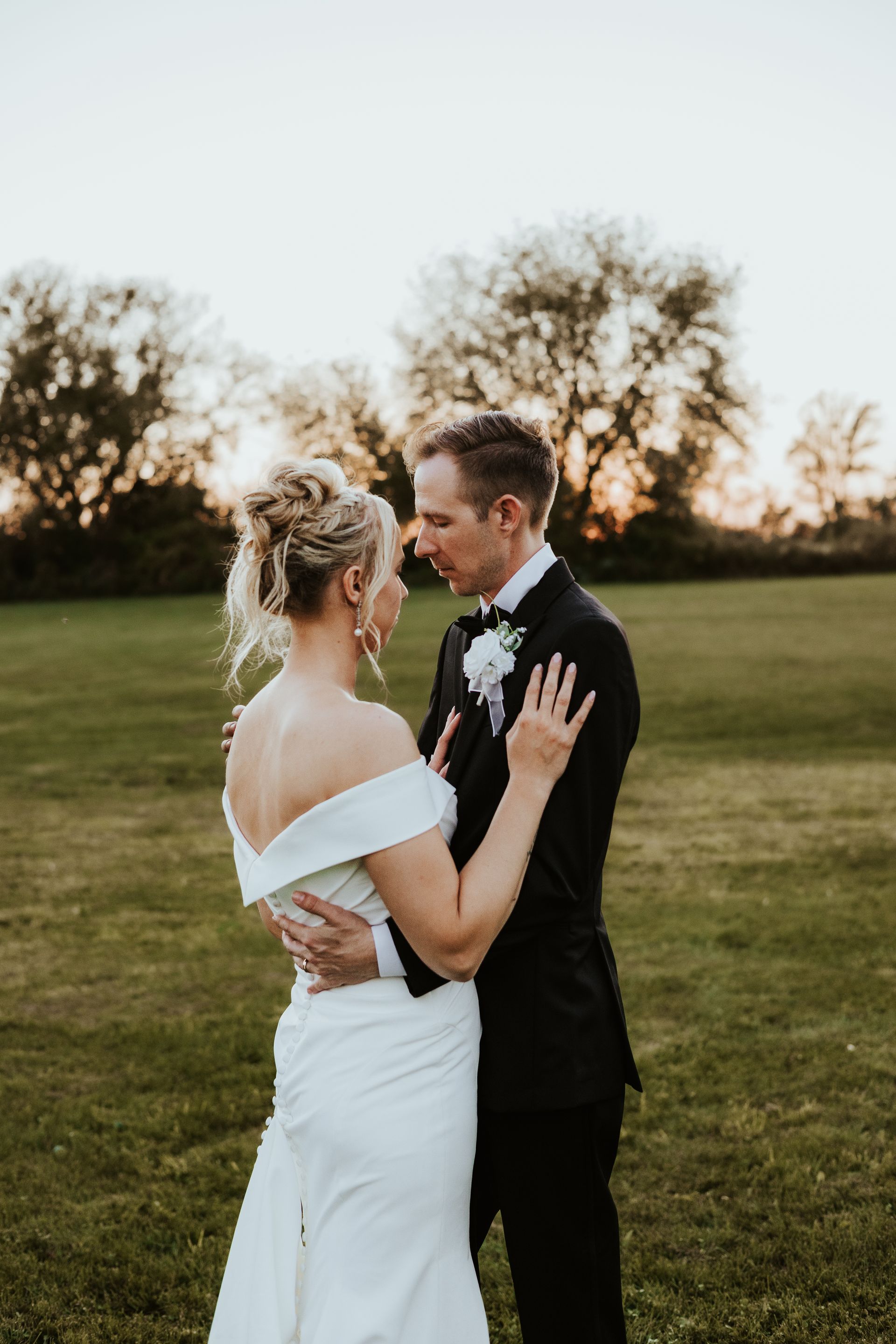 A bride and groom are standing in a field looking at each other.