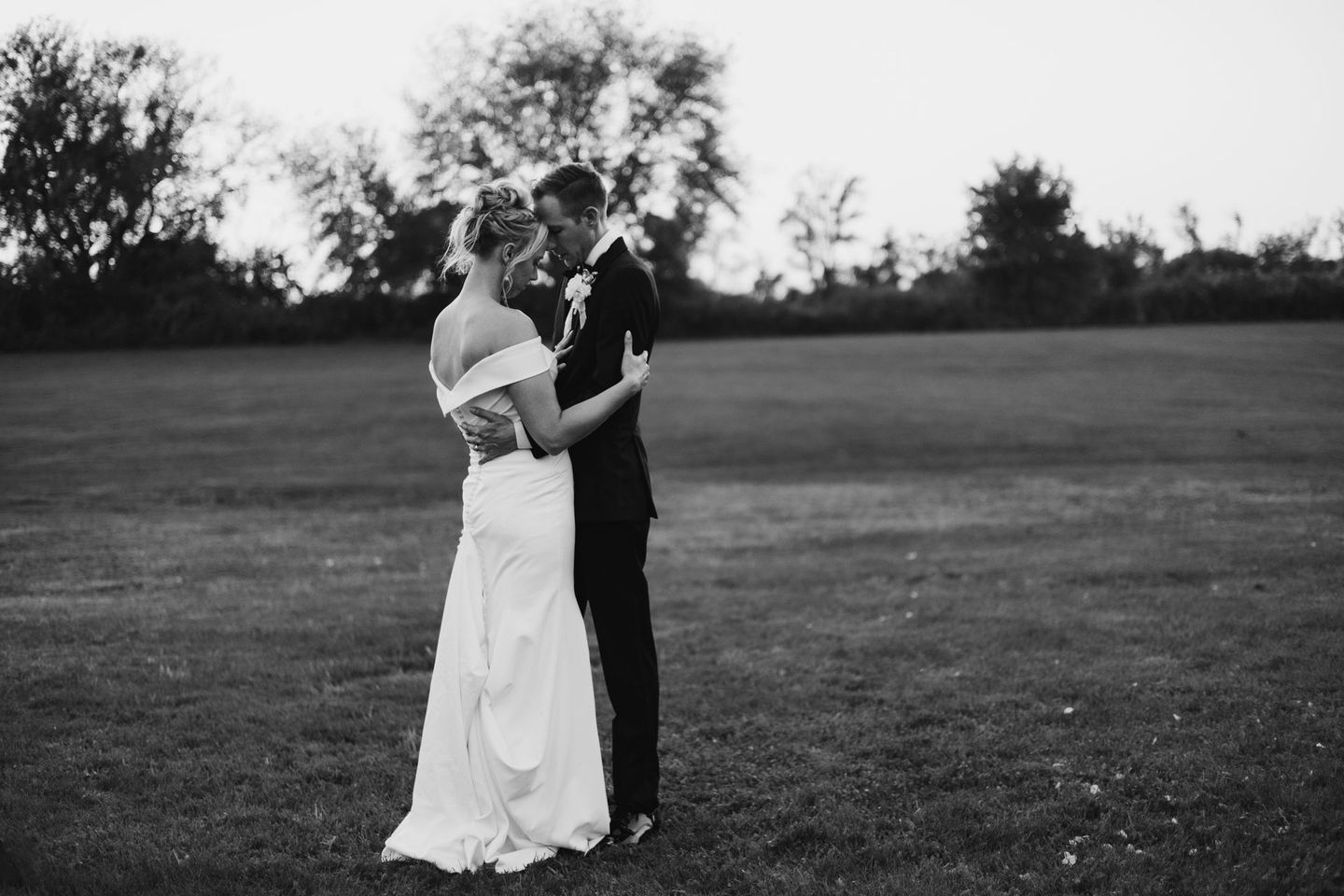 A black and white photo of a bride and groom hugging in a field.