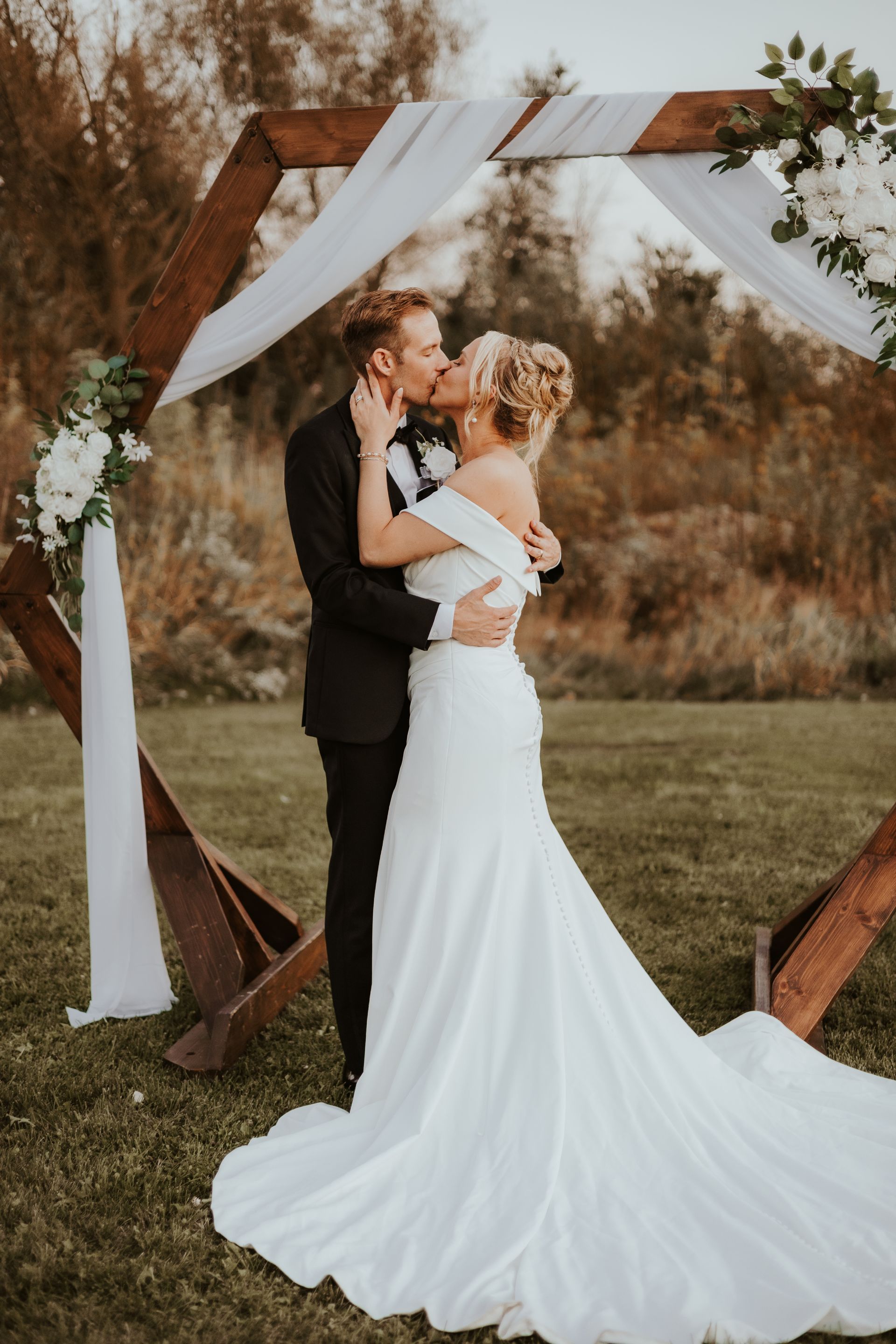 A bride and groom are kissing under a wooden arch.