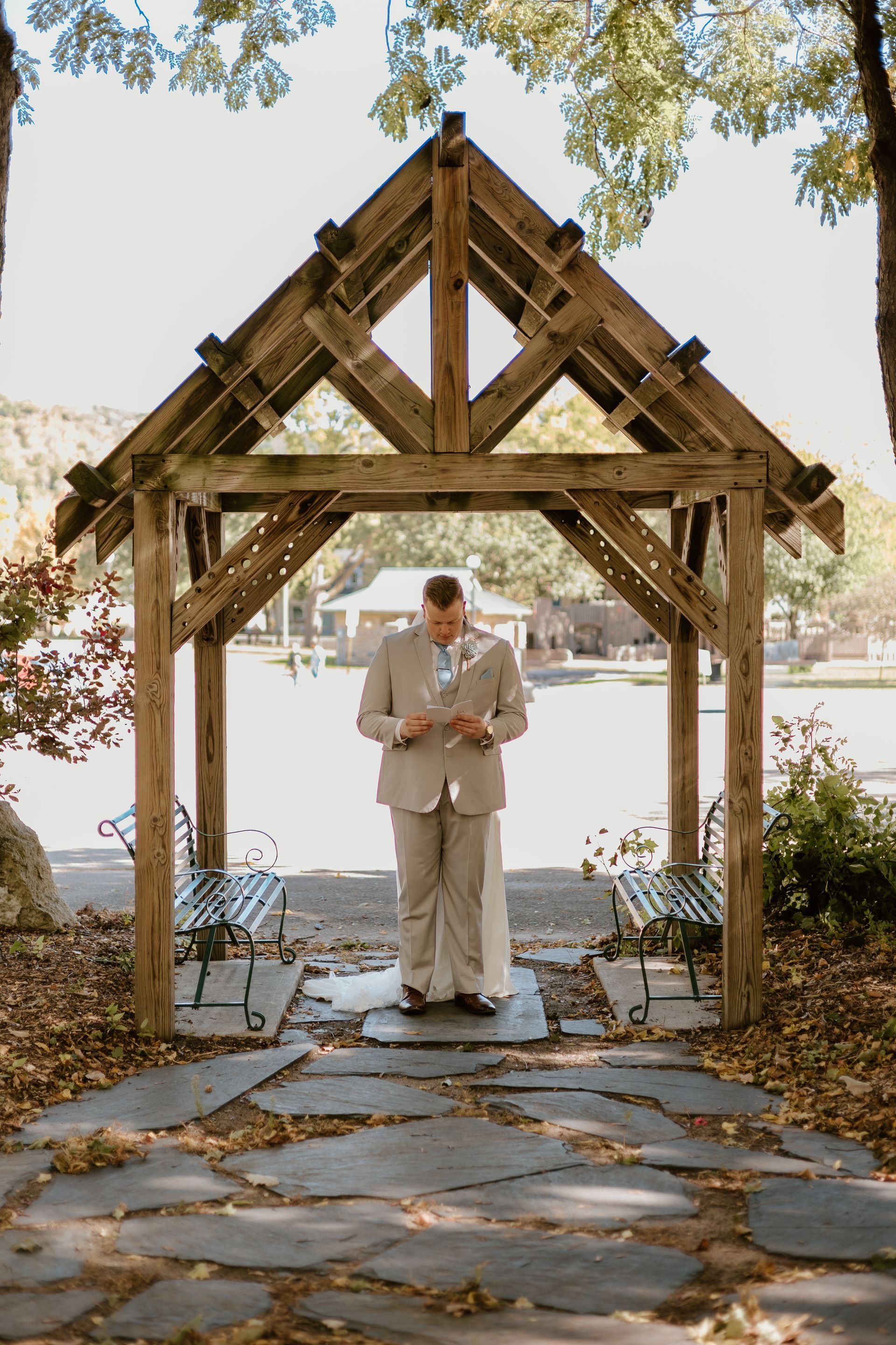 A bride and groom are standing under a wooden gazebo.