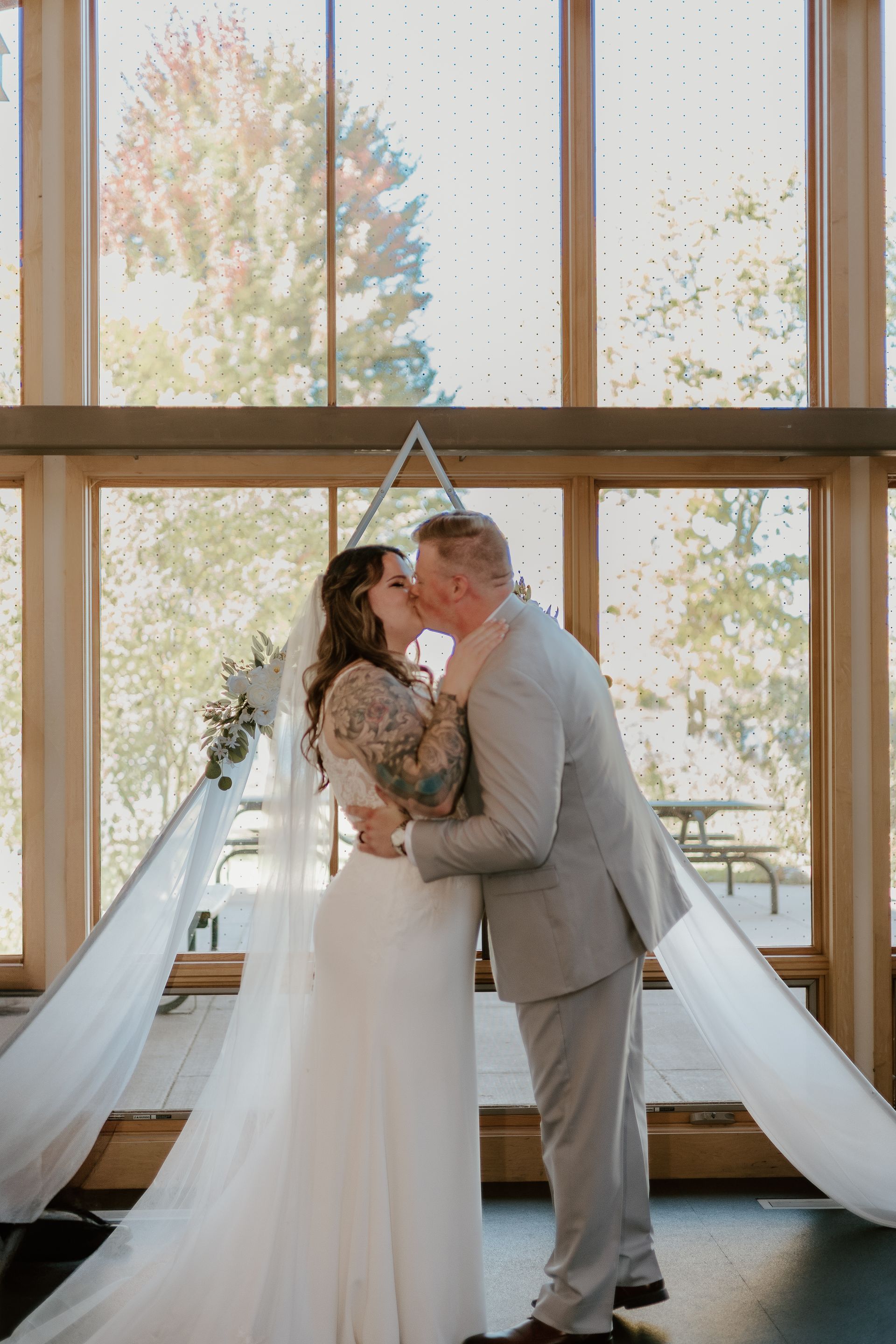 A bride and groom are kissing in front of a large window.