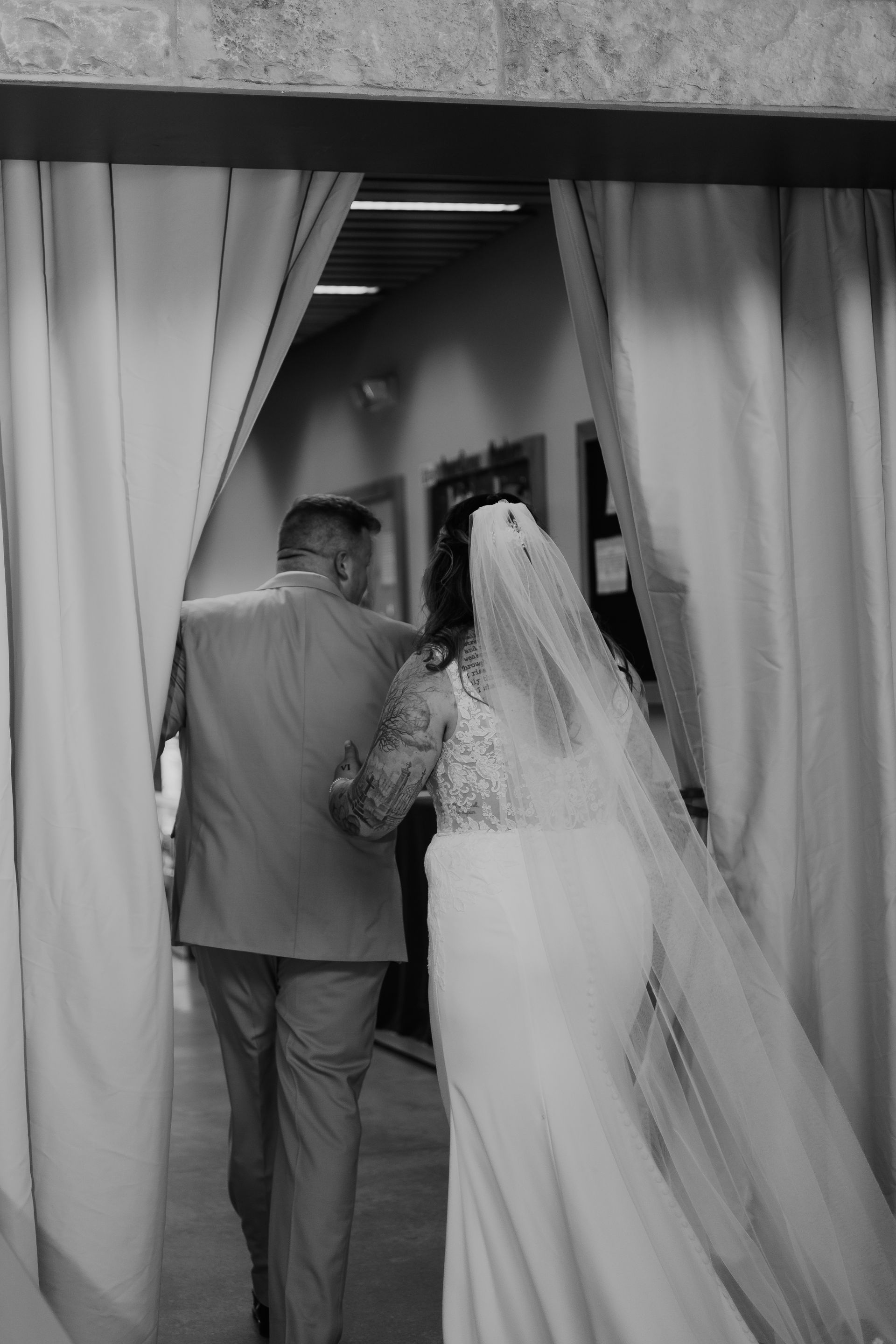 A black and white photo of a bride walking down the aisle with her father.