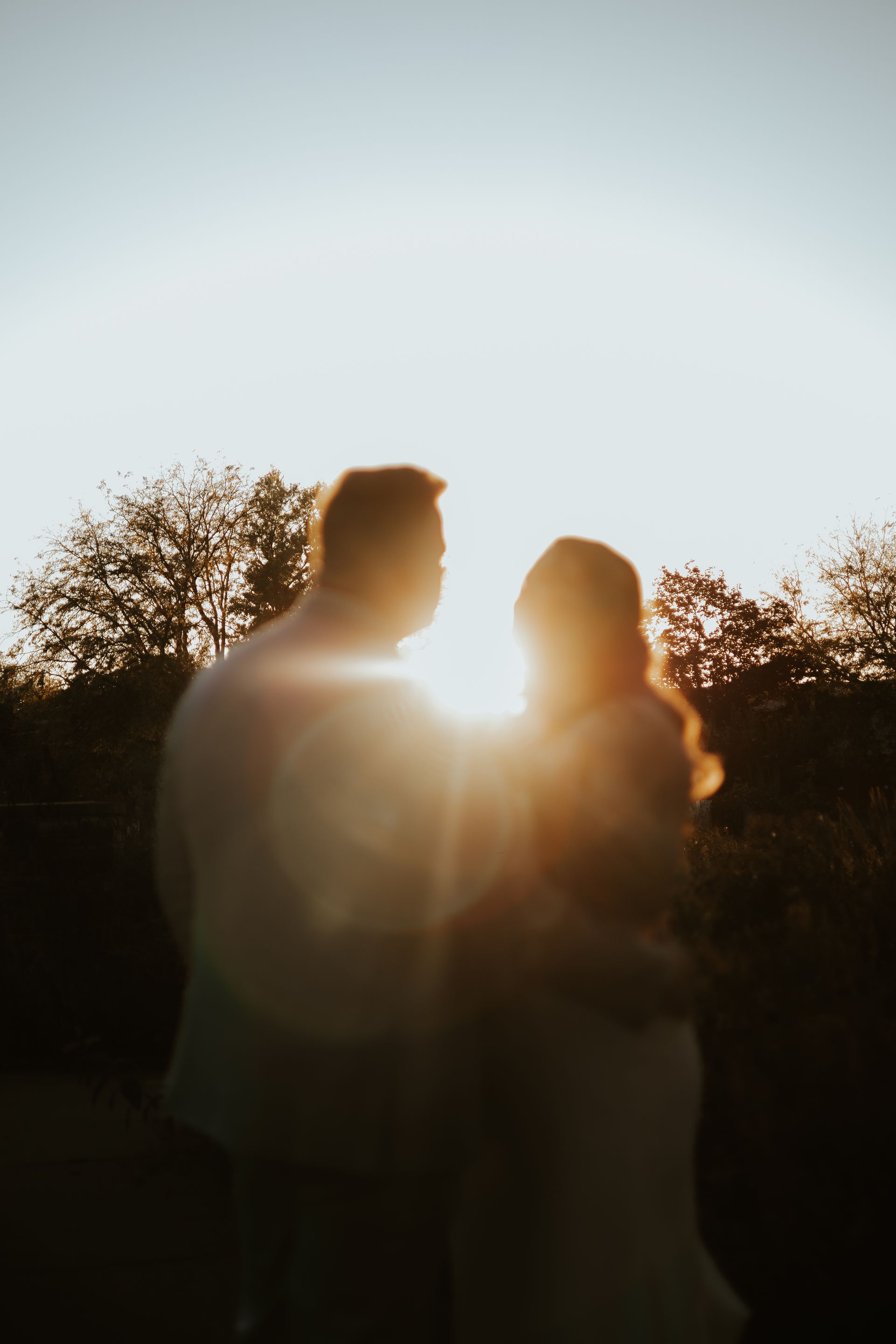 A man and a woman are standing next to each other in front of a sunset.