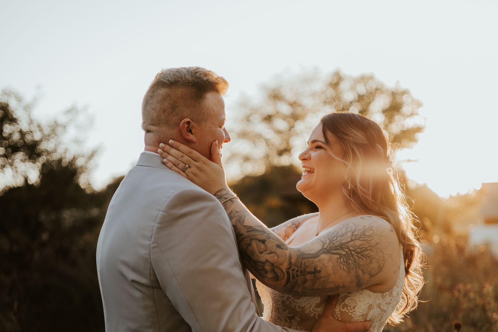 A bride and groom are standing next to each other in a field at sunset.