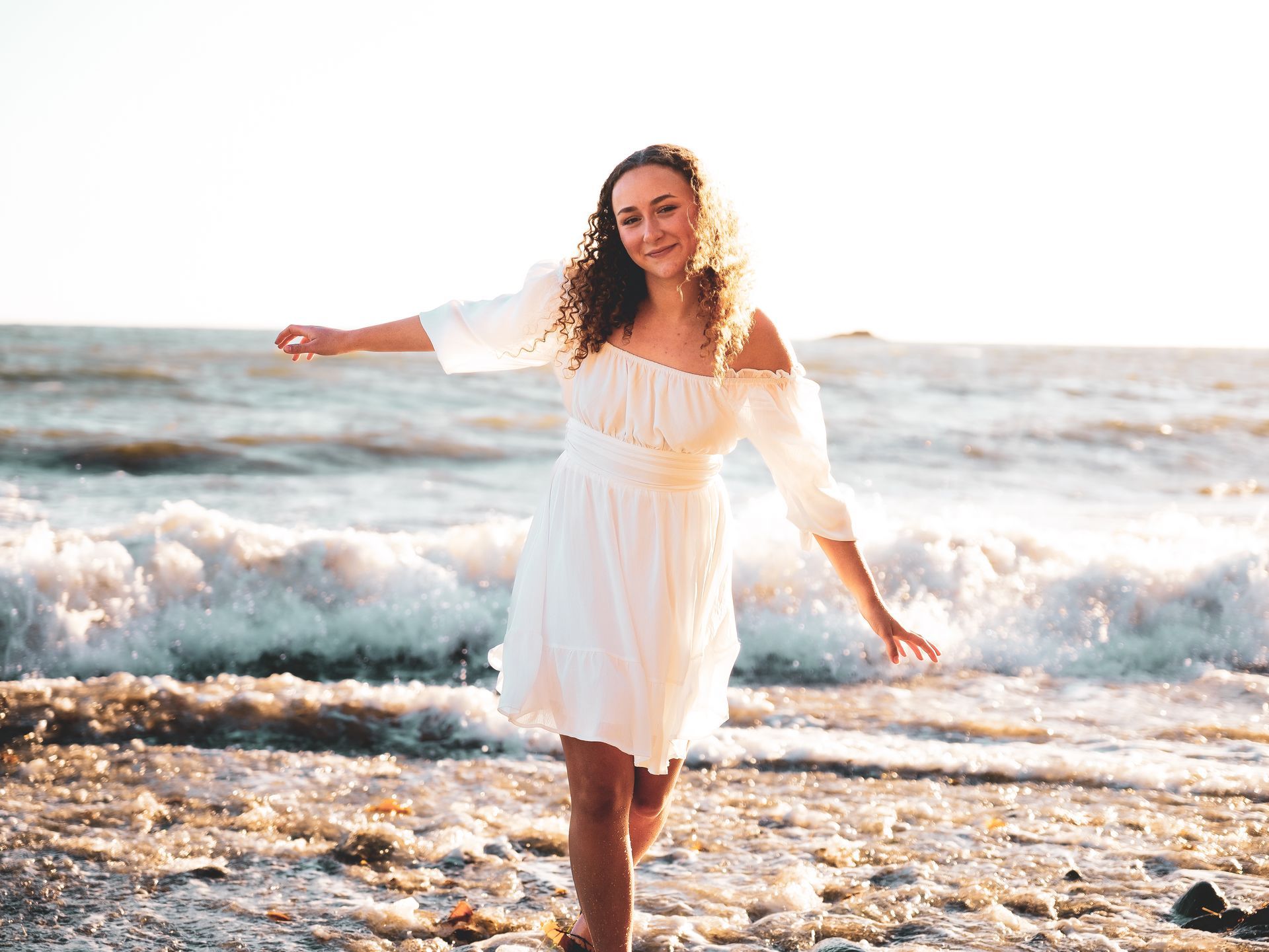 A woman in a white dress is walking on the beach.