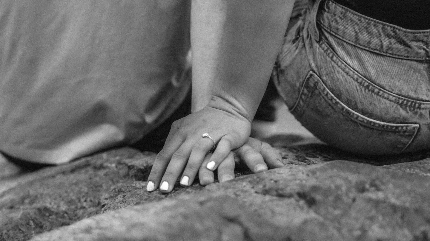 A black and white photo of a person holding a baby 's hand on a rock.