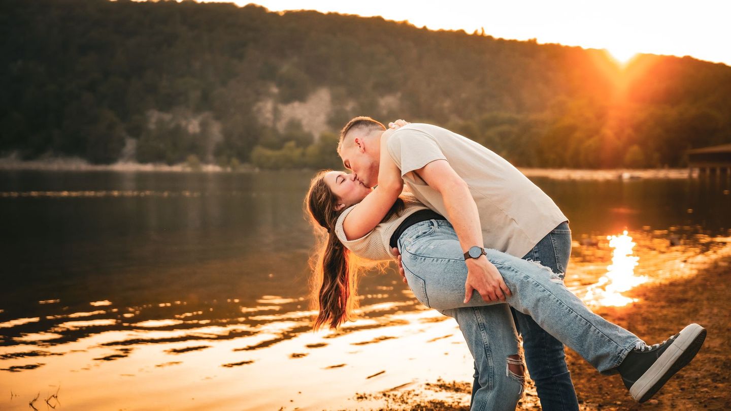 A man is holding a woman in his arms and kissing her on the beach.