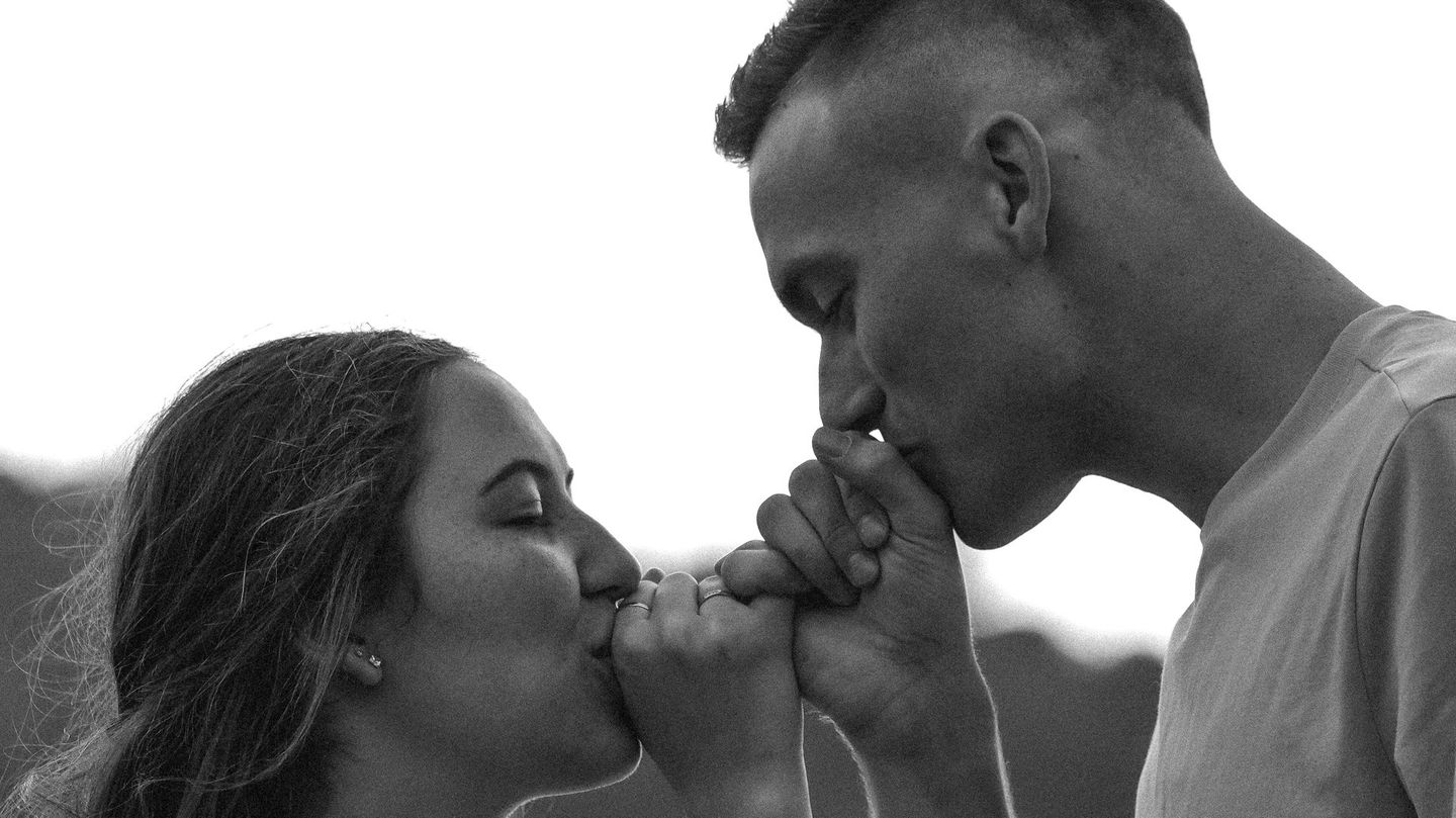 A man and a woman are kissing each other 's hands in a black and white photo.