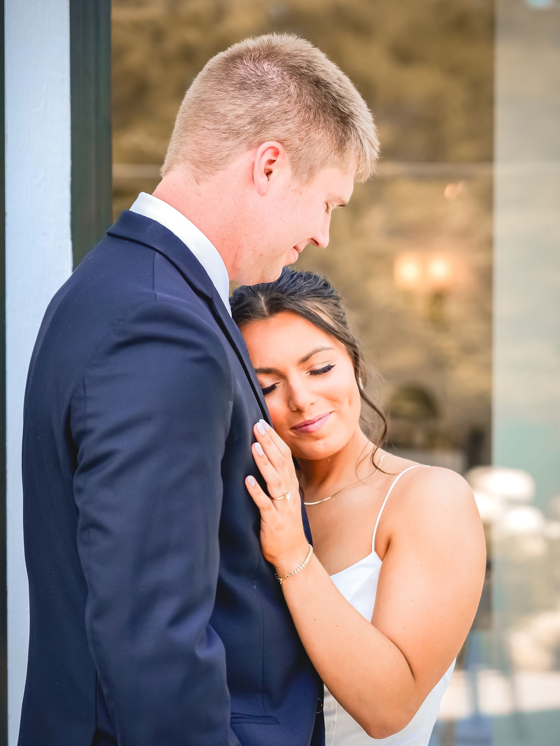A bride and groom are hugging each other in front of a window.