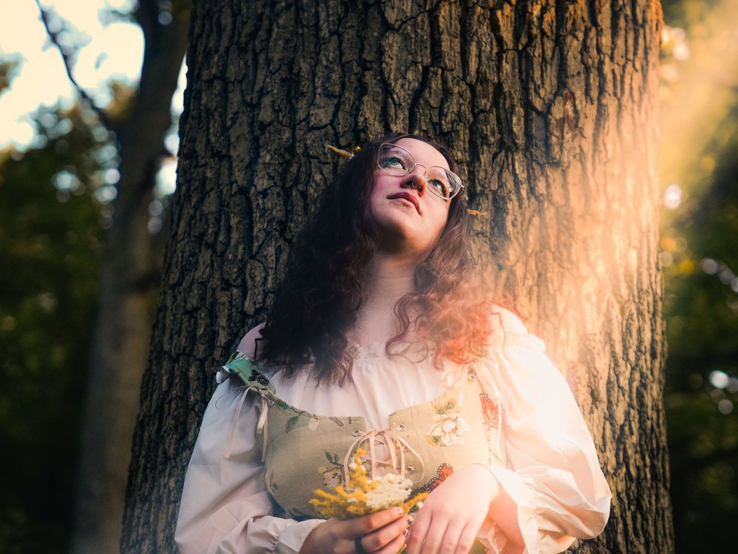 A woman is leaning against a tree holding a bouquet of flowers.