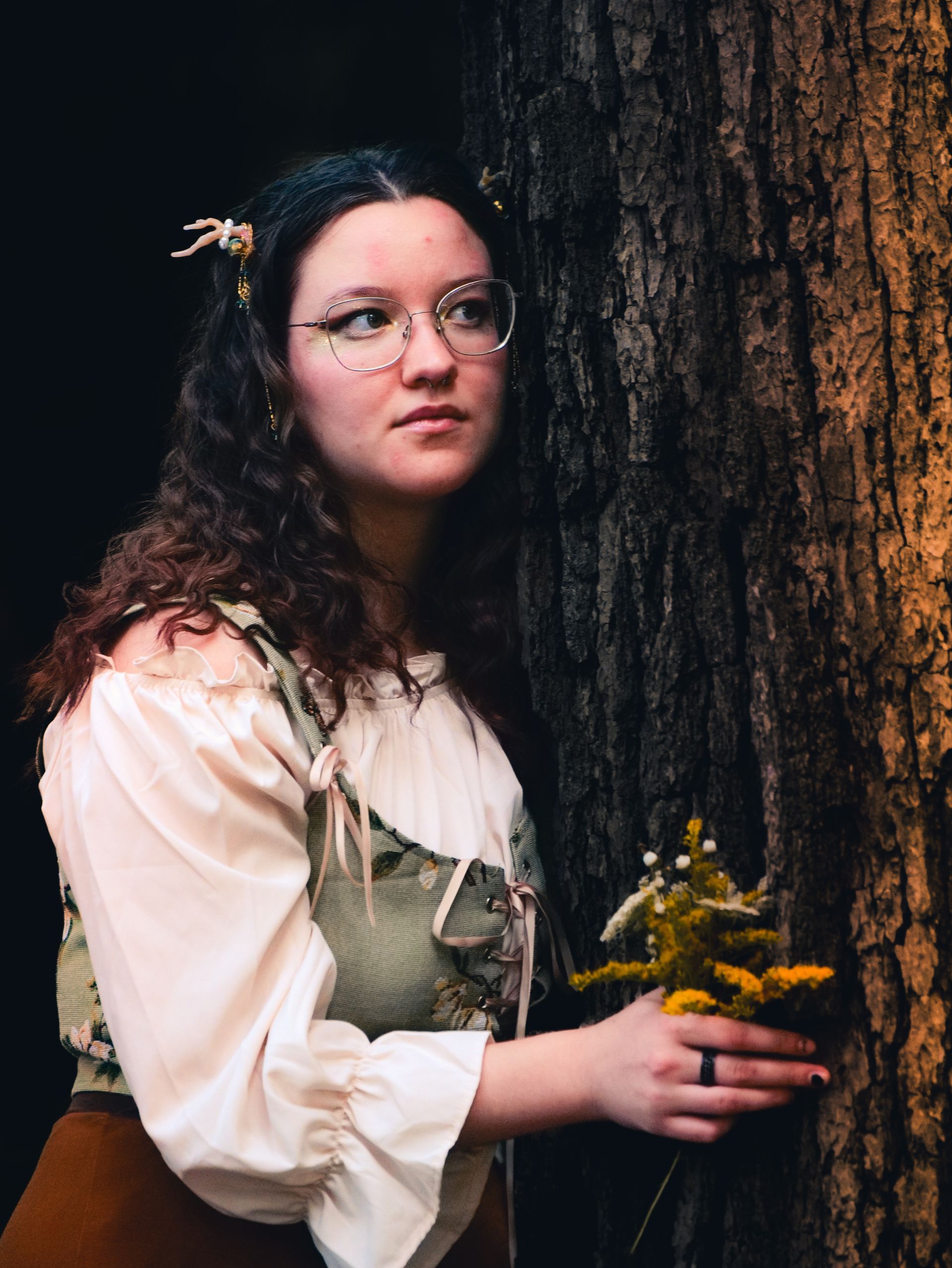 A woman is standing next to a tree holding flowers.