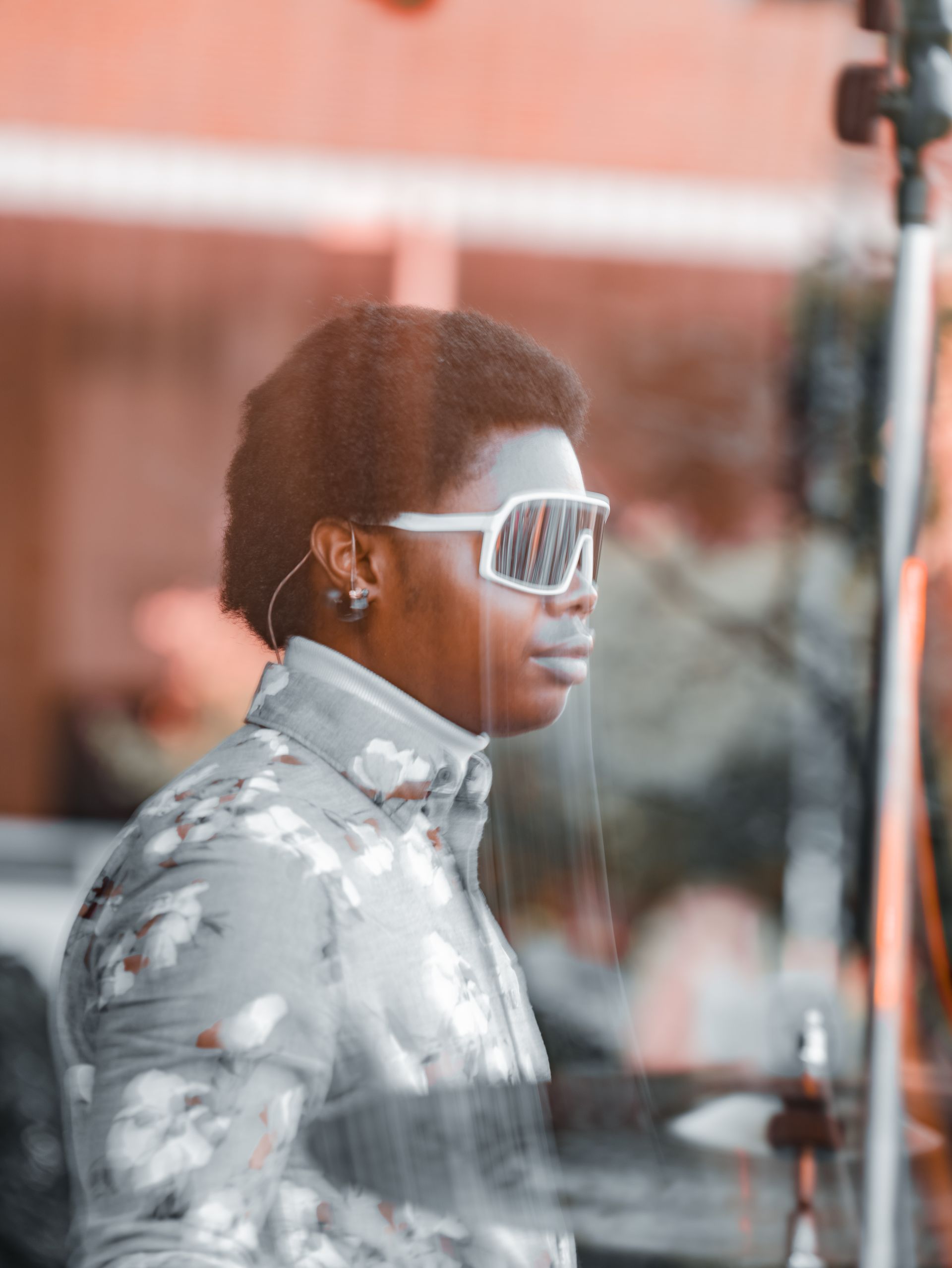 A man wearing sunglasses and a floral shirt is standing in front of a mirror.