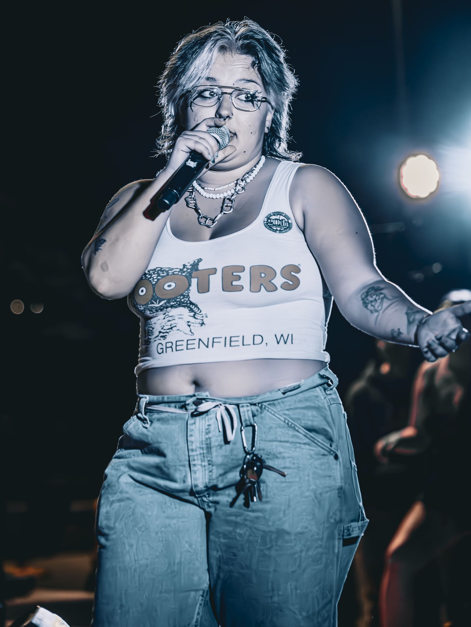A woman in a hooters tank top is singing into a microphone.