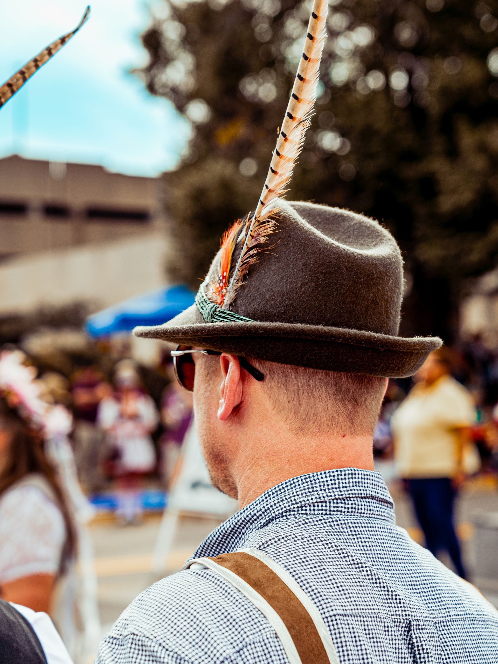 A man wearing a hat with feathers on it is standing in front of a crowd.