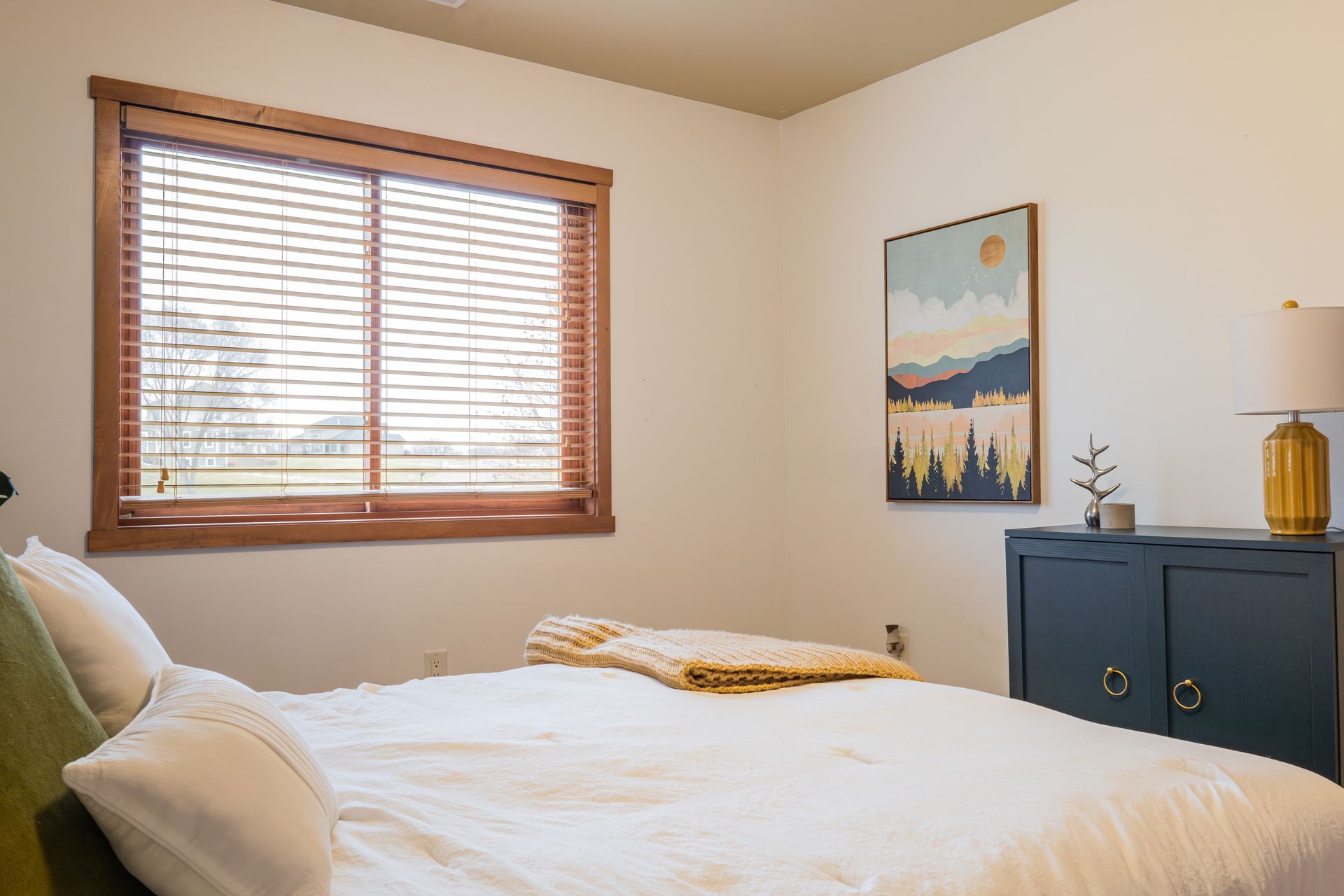 A bedroom with a bed , dresser , lamp and window.