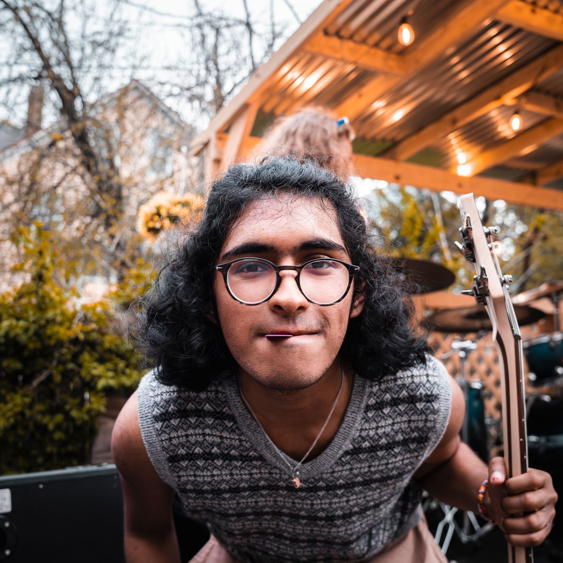 A young man wearing glasses is holding a guitar and sticking his tongue out.