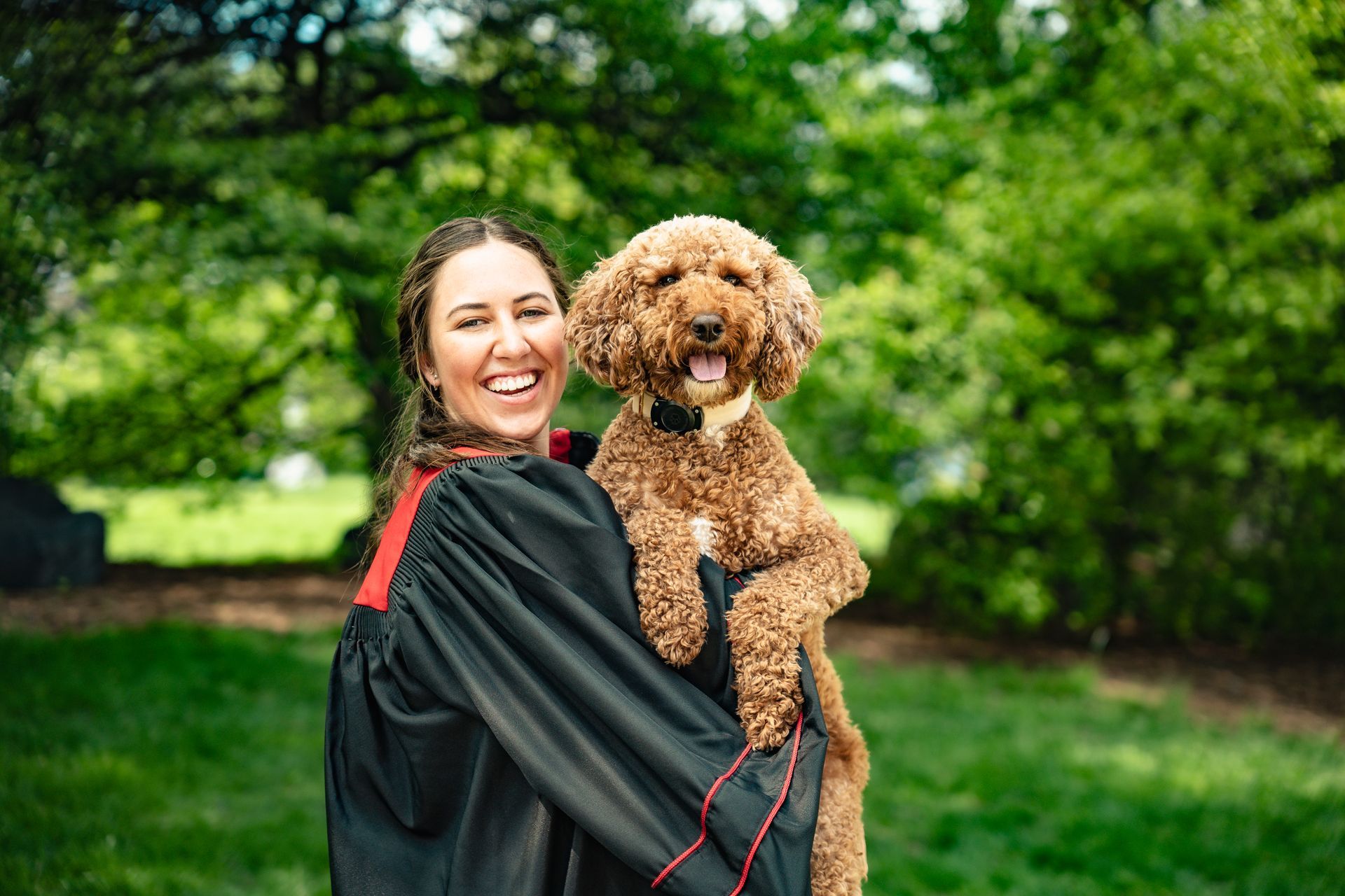 A woman in a graduation cap and gown is holding a brown dog.
