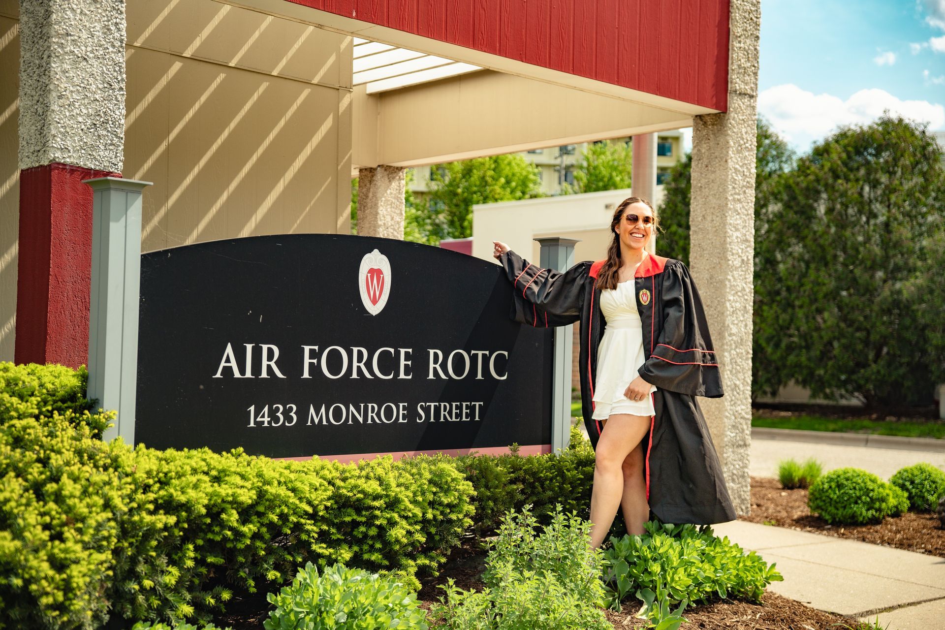 A woman in a graduation cap and gown is standing in front of a sign for the air force rotc.