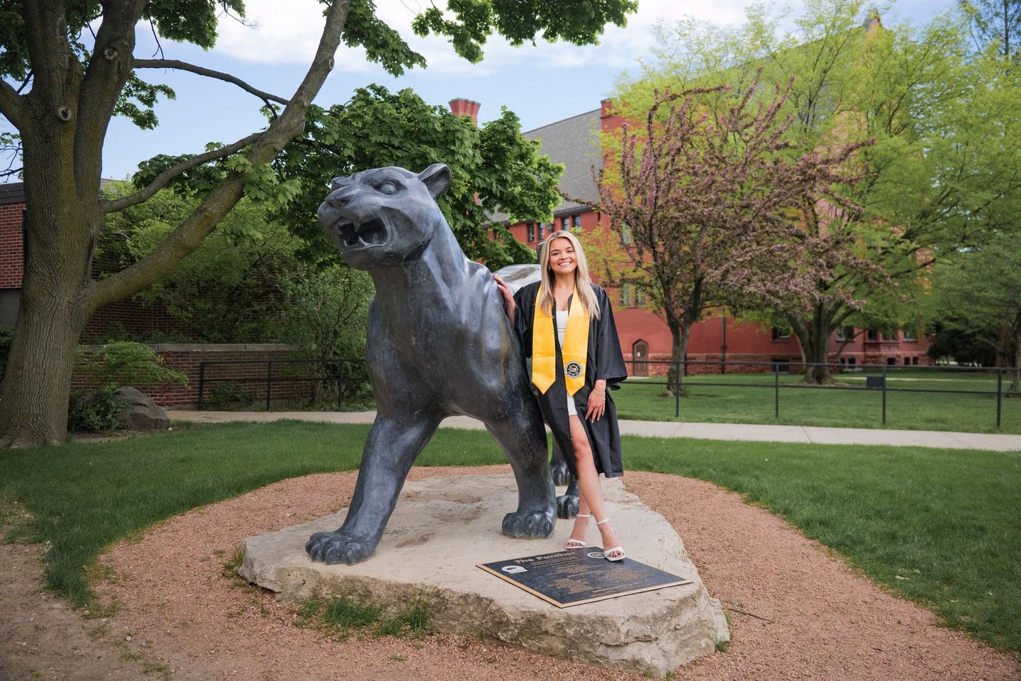 A woman in a cap and gown is standing next to a statue of a panther.