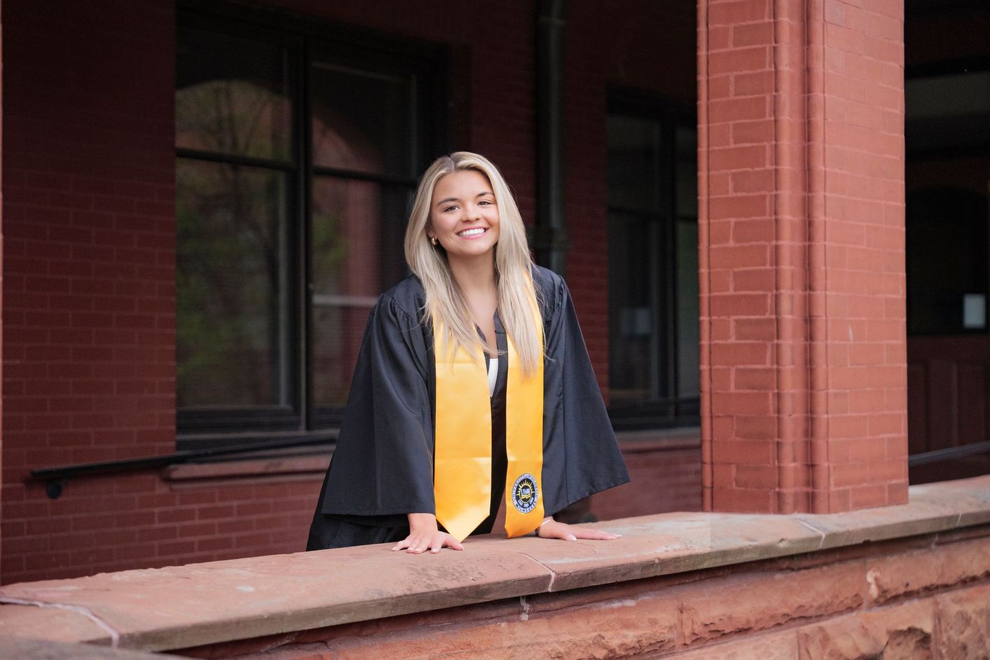 A woman in a graduation cap and gown is standing on a porch.