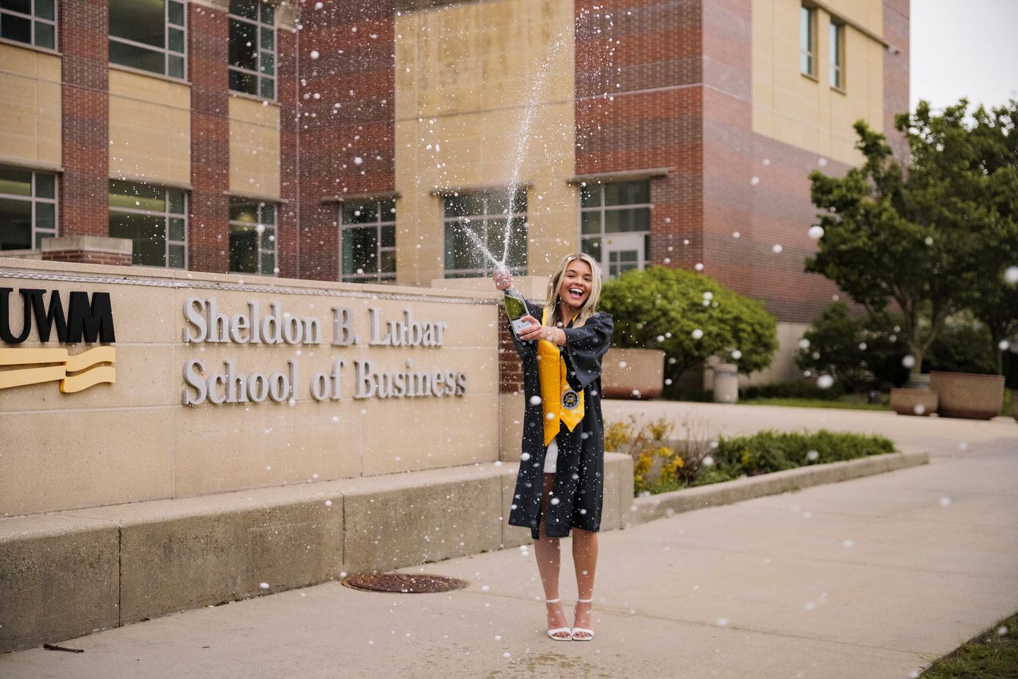 A woman in a graduation cap and gown is spraying champagne