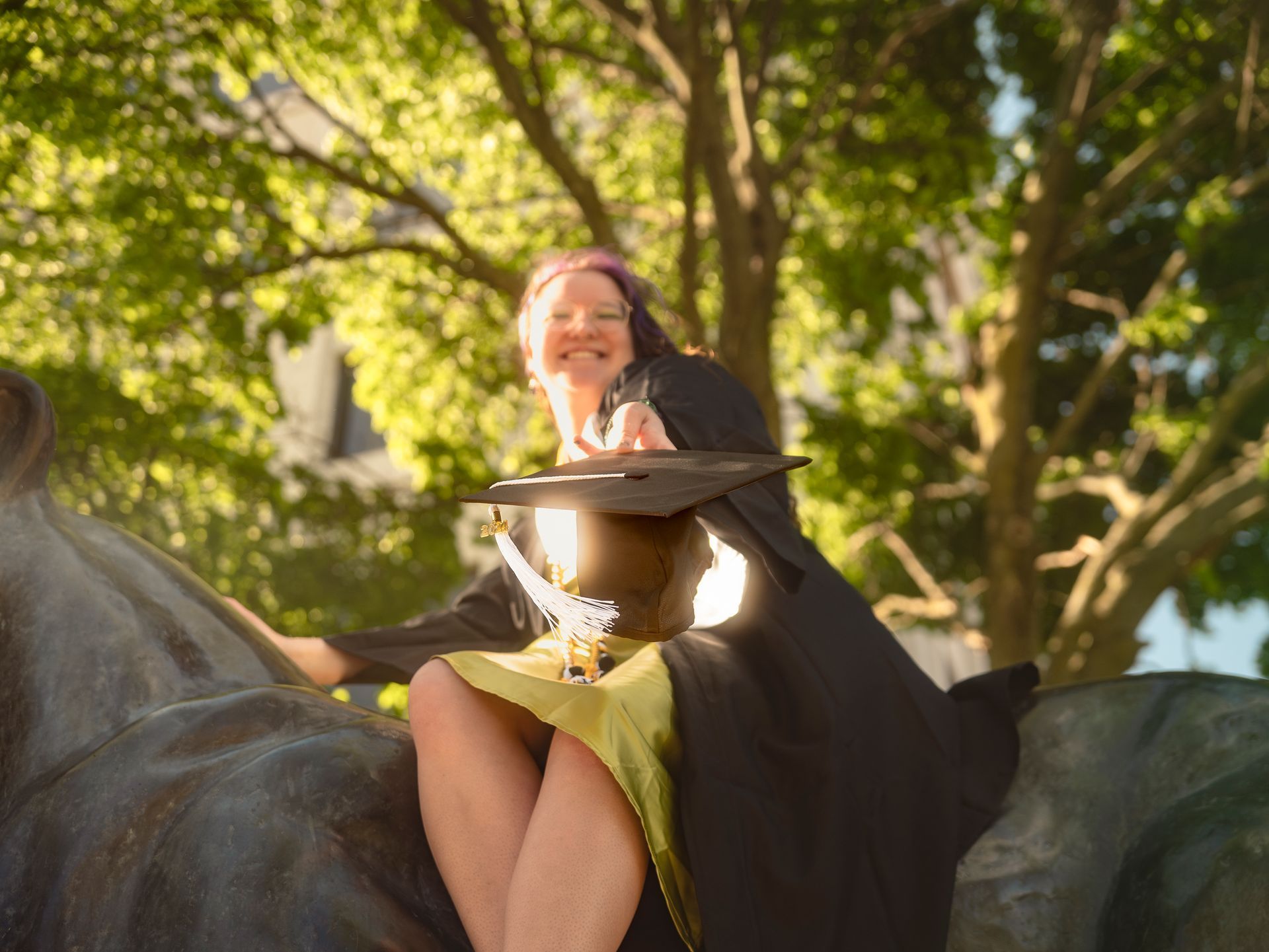 A woman in a graduation cap and gown is sitting on a statue of a horse.