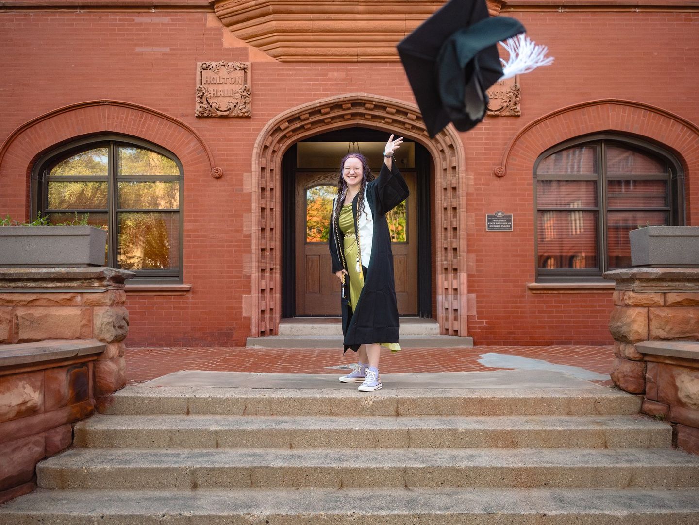 A woman in a graduation cap and gown is throwing her cap in the air.