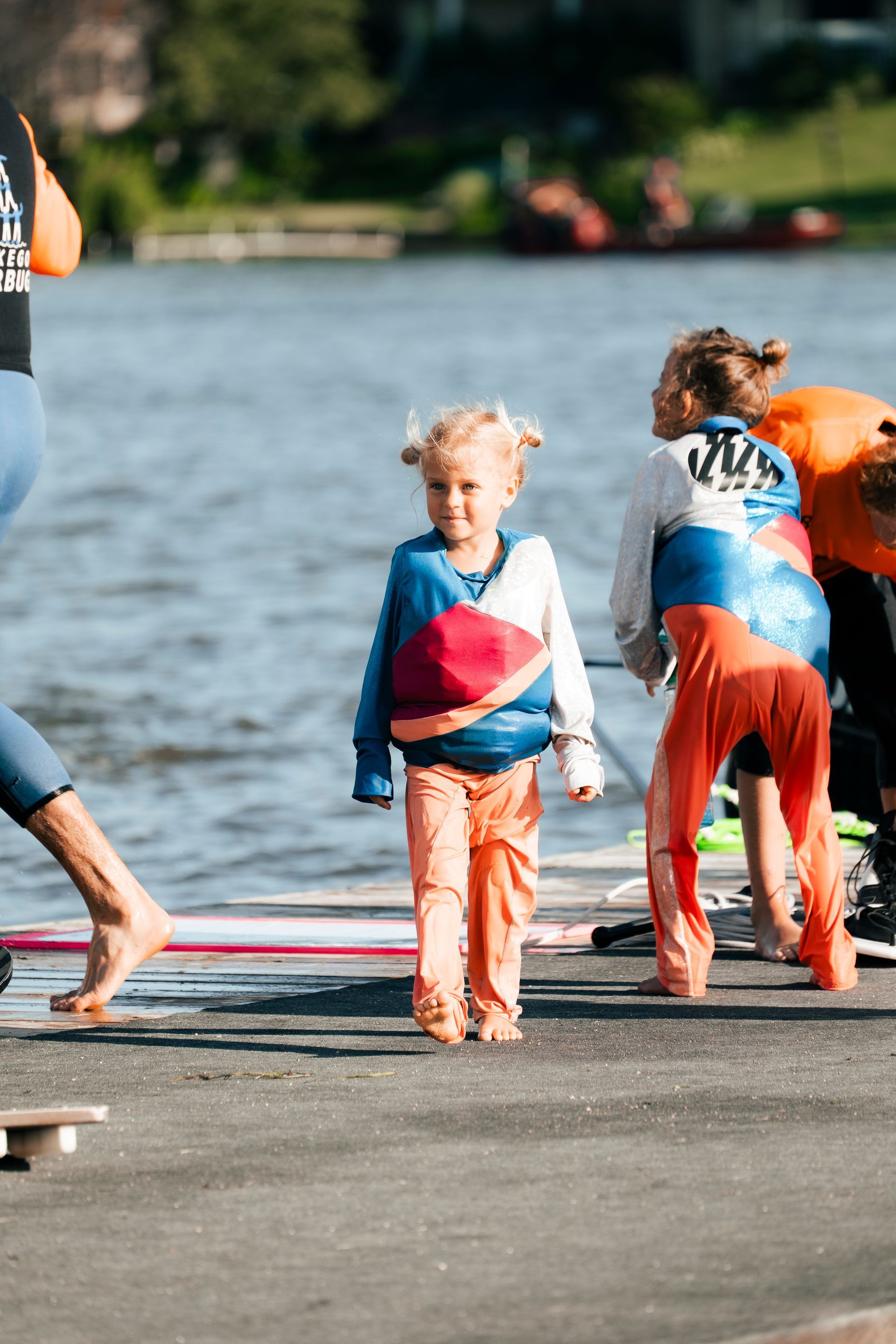 A group of children are standing on a dock near a body of water.