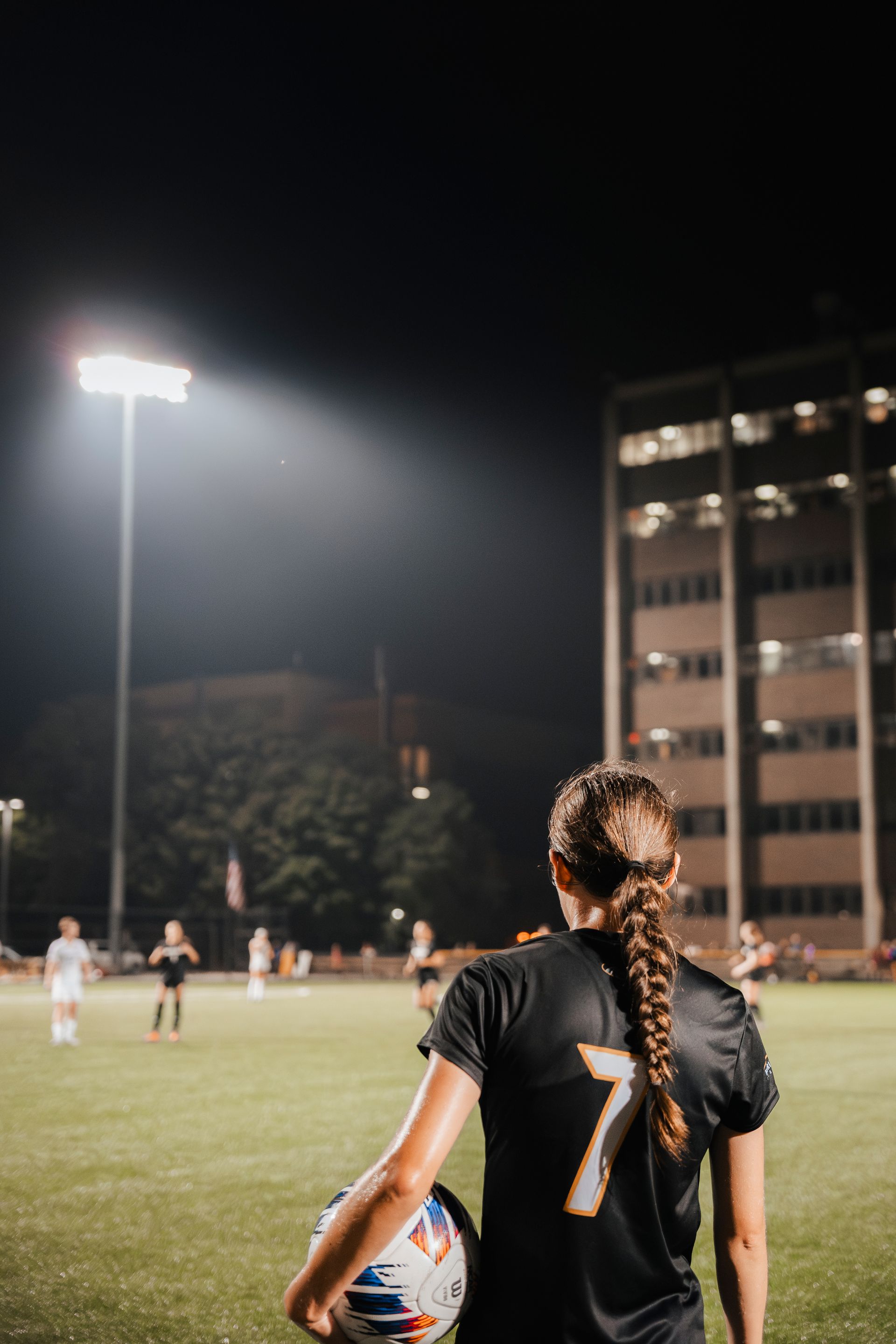 A woman is holding a soccer ball on a field at night.