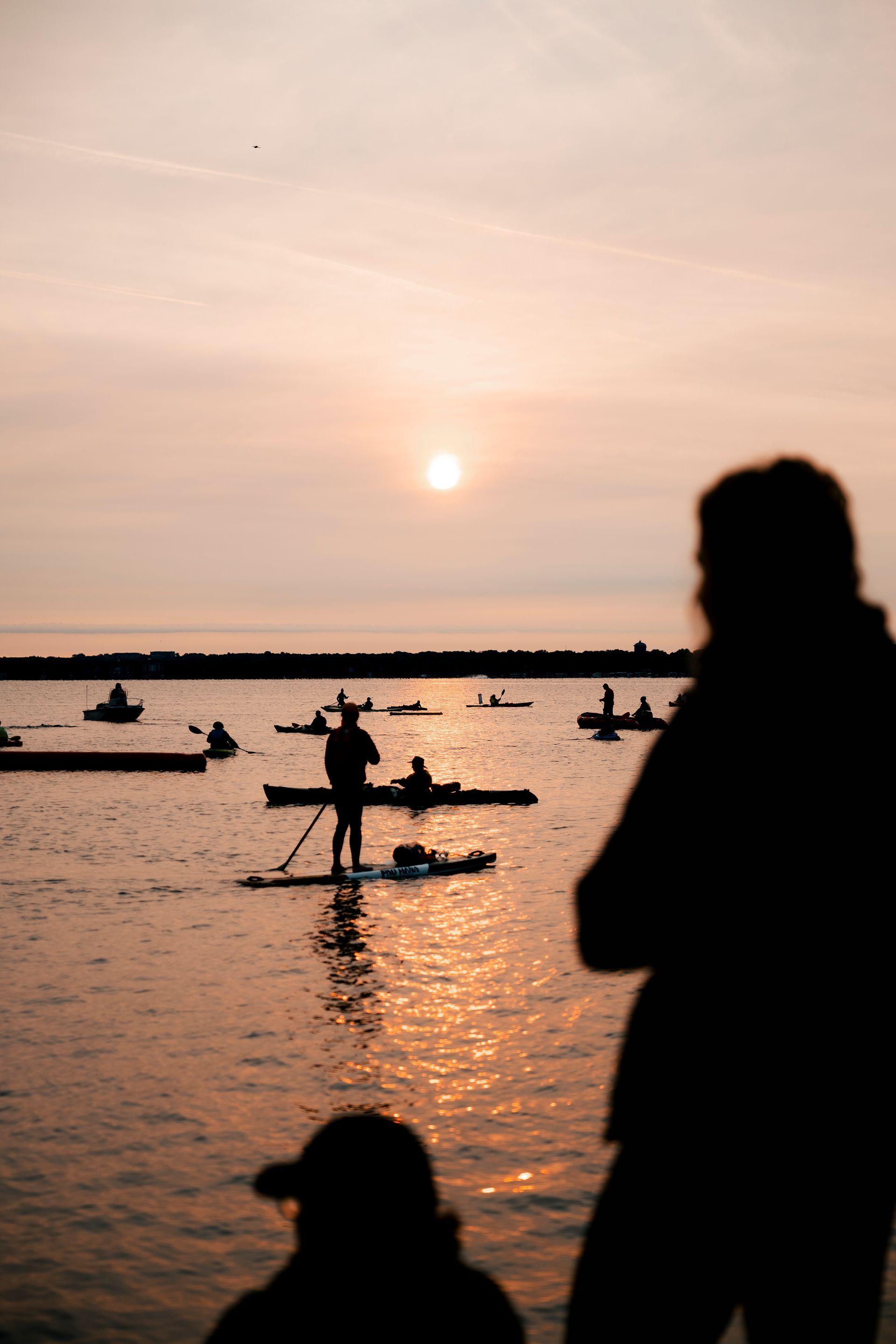 A group of people are standing on paddle boards in the water at sunset.
