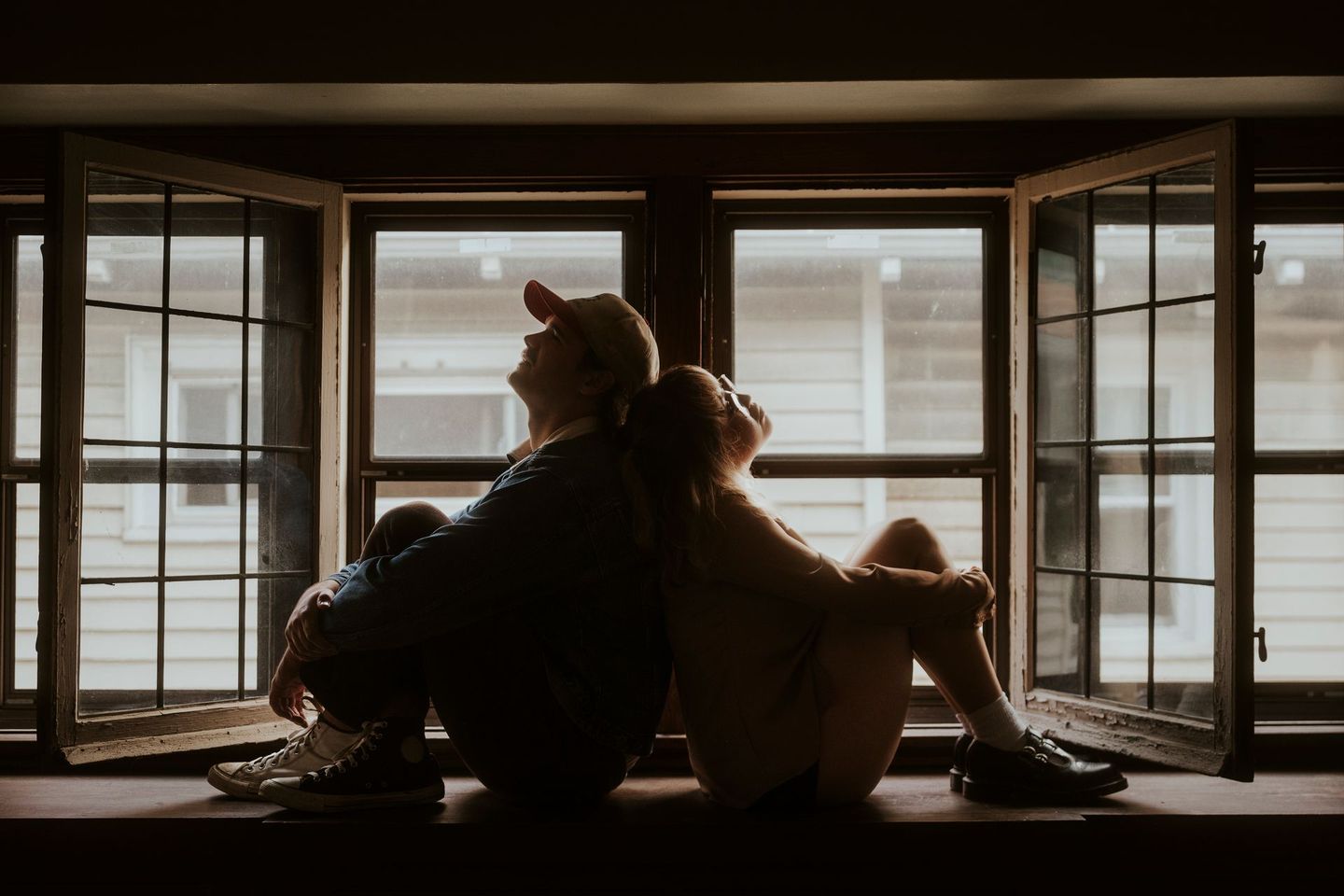 A man and a woman are sitting back to back on a window sill.