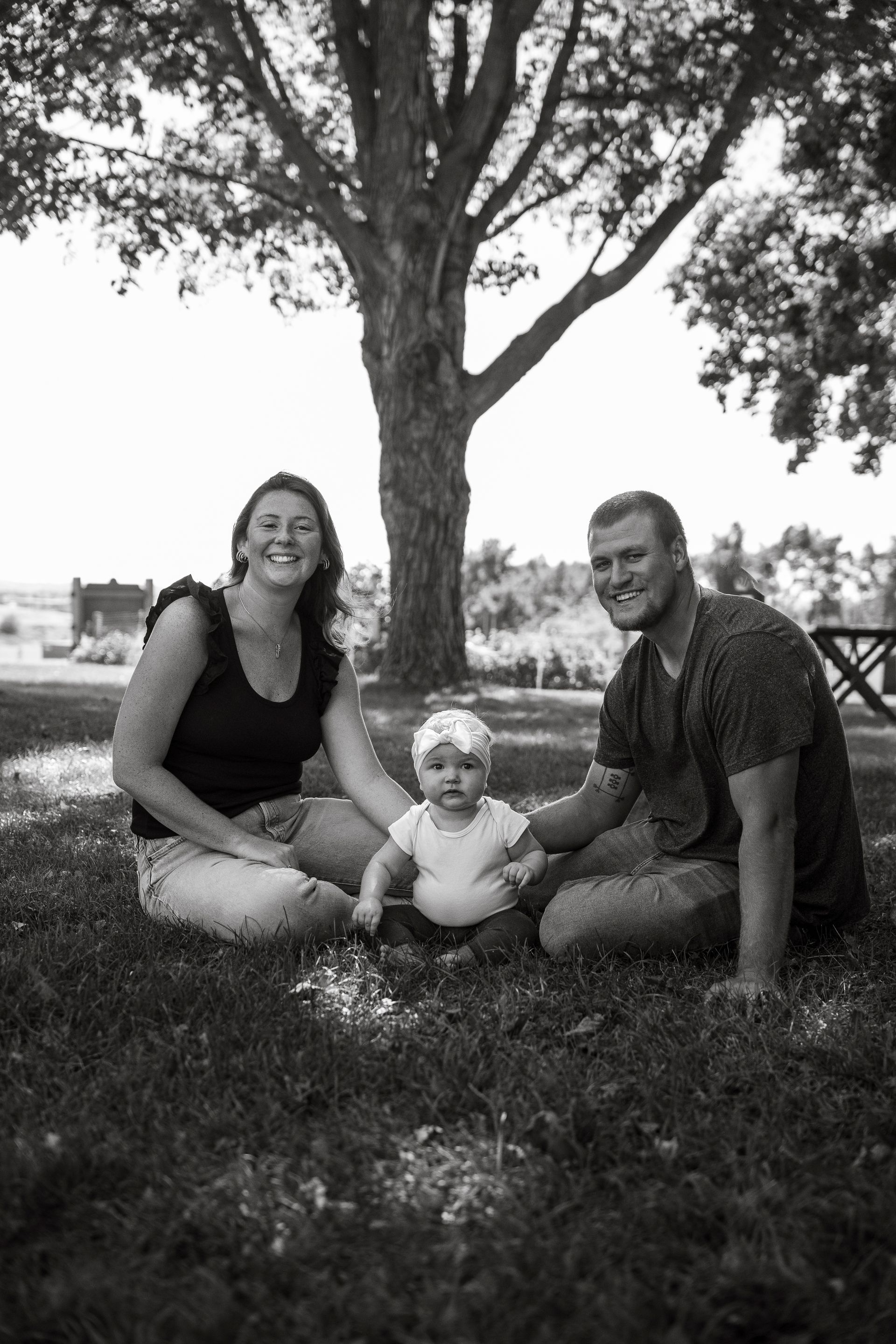 A black and white photo of a family sitting in the grass under a tree.