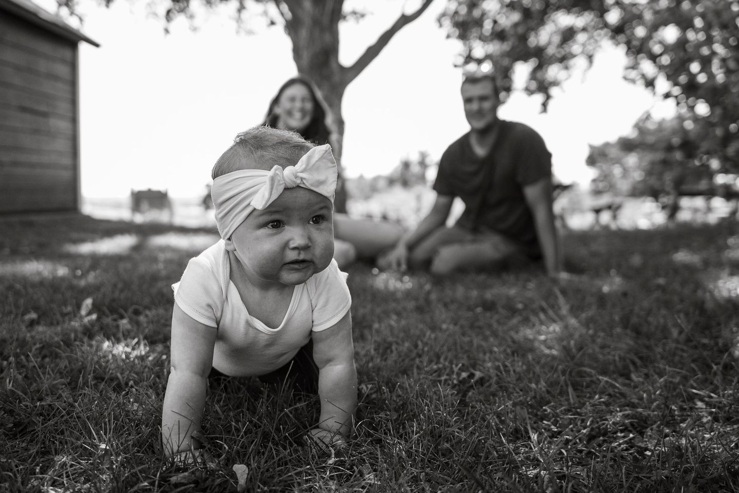 A black and white photo of a baby crawling in the grass.