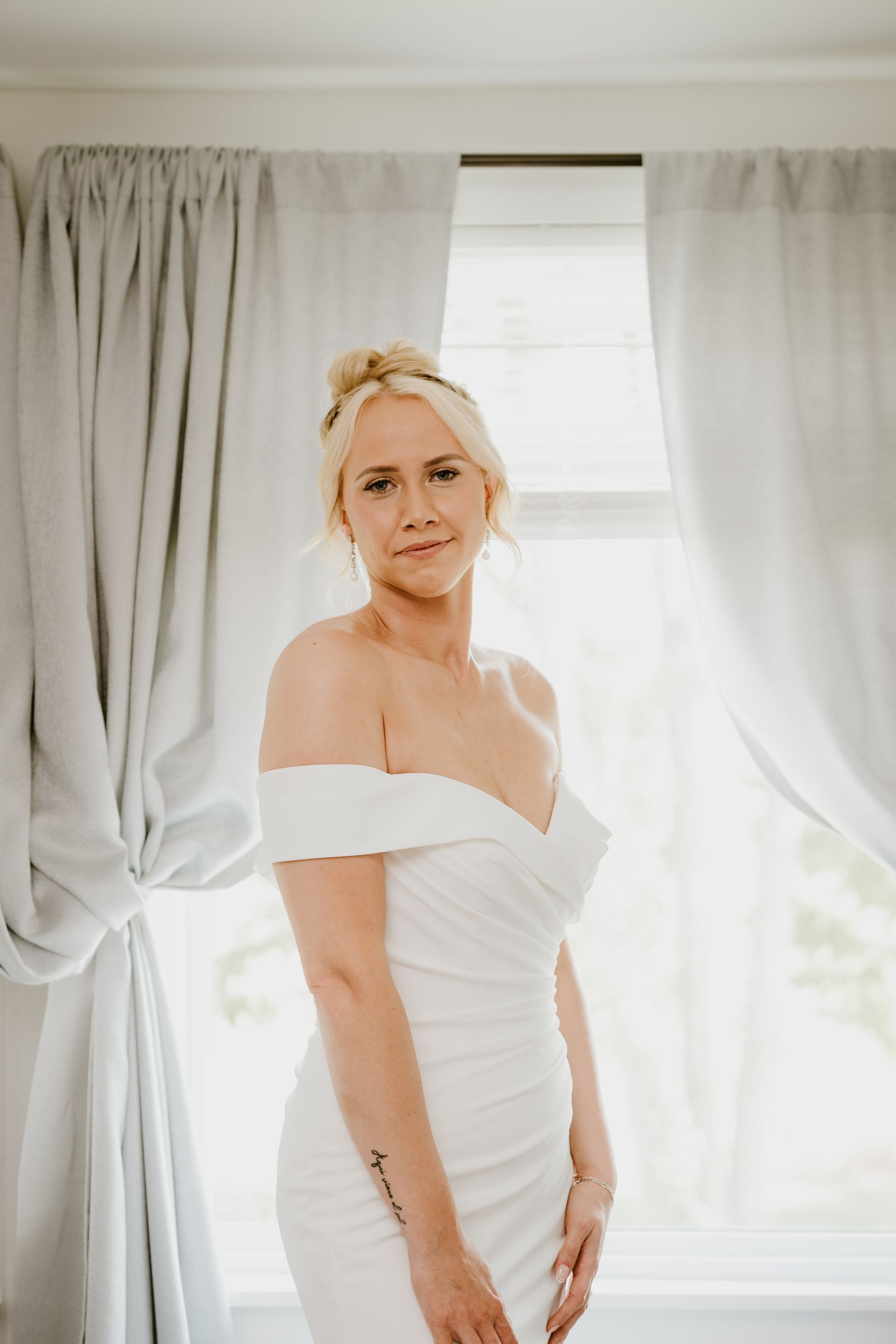 A woman in a white dress is standing in front of a window.