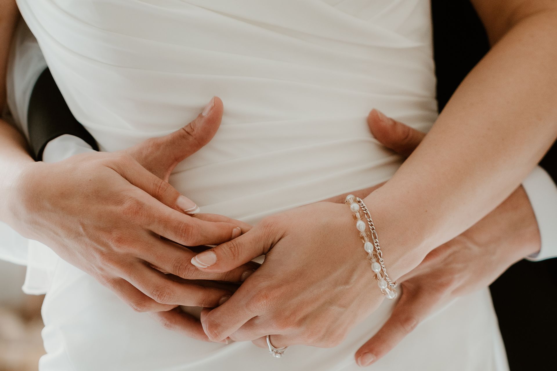 A bride and groom are hugging each other while the bride is wearing a bracelet.