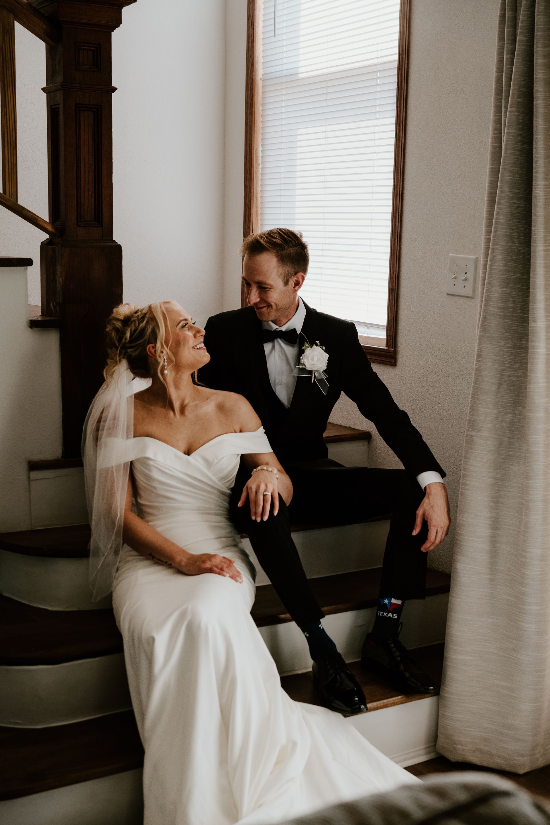 A bride and groom are sitting on the stairs in front of a window.