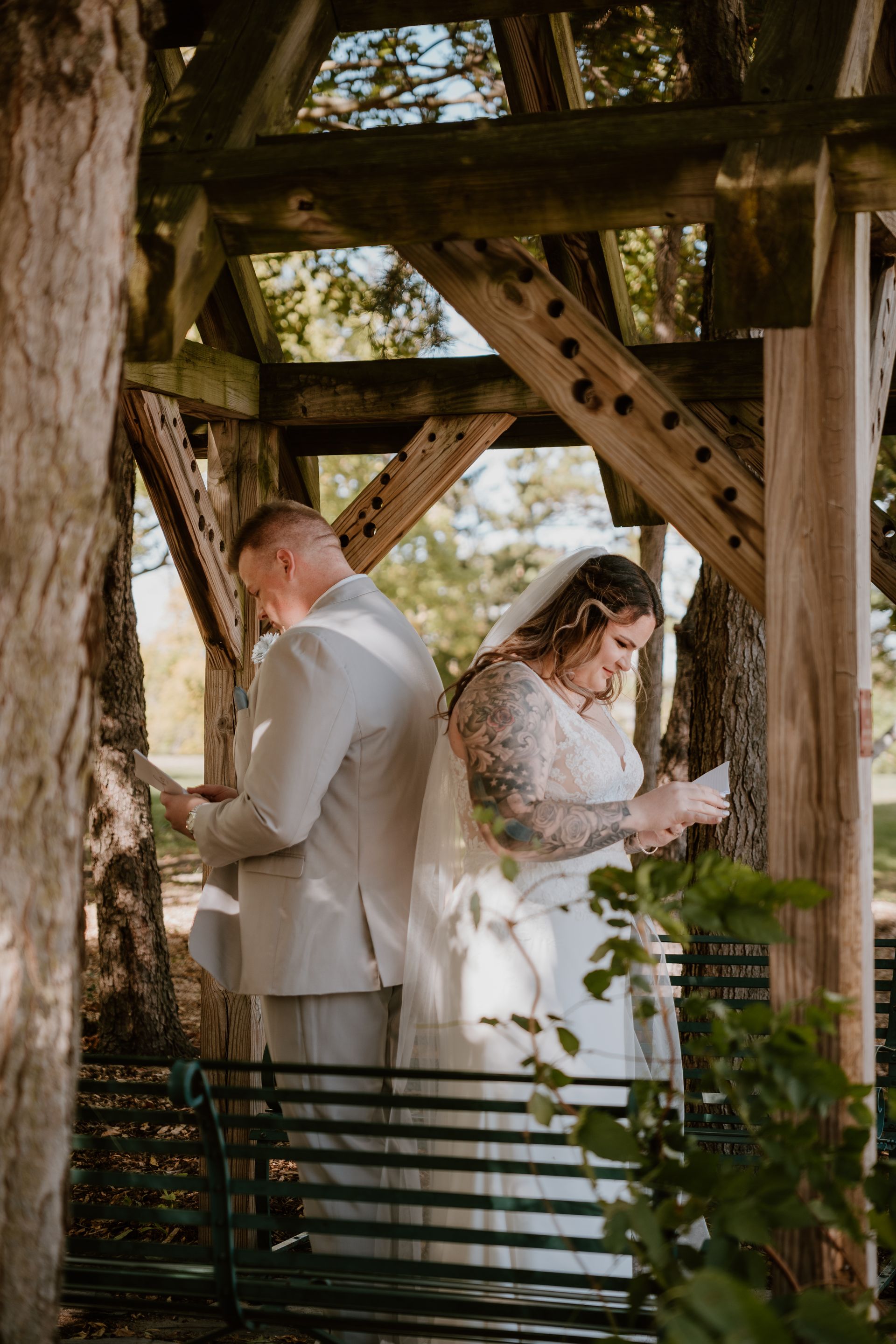 A bride and groom are standing under a wooden structure.